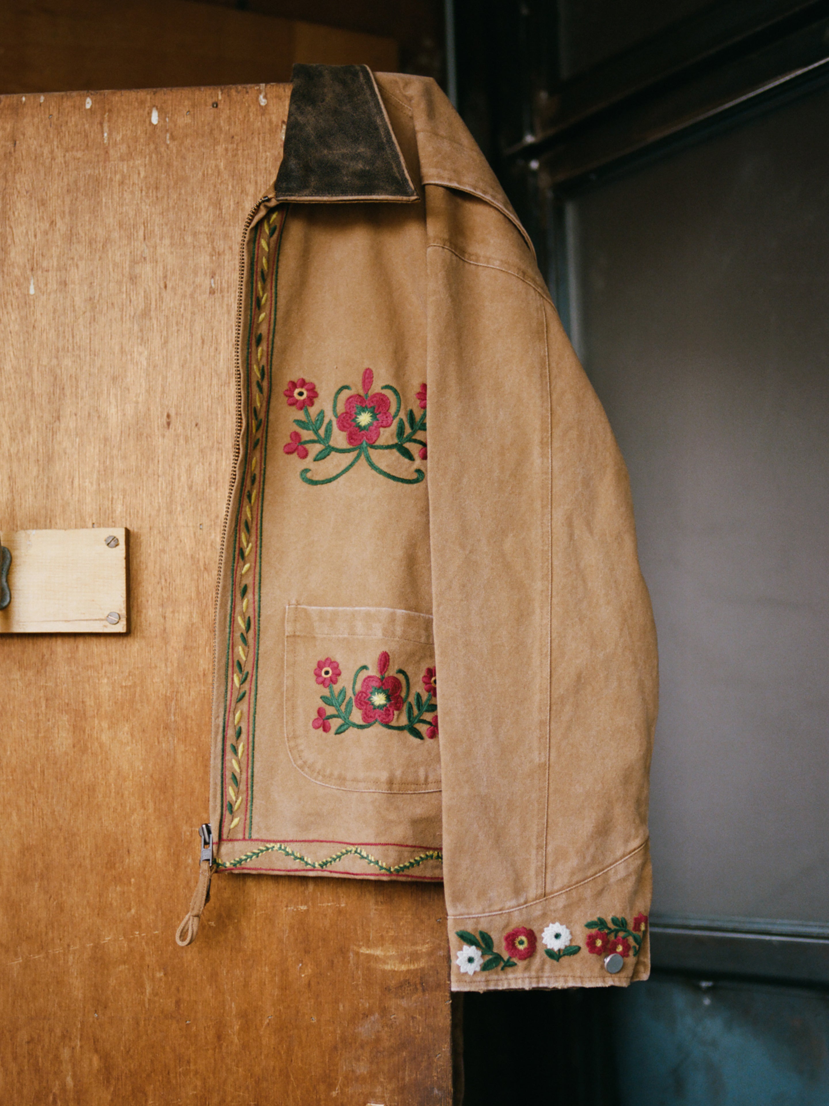 The Found Rosette Canvas Work Jacket, a vintage brown piece, features floral embroidery on the sleeve and chest. A darker collar adds contrast, making this jacket a unique addition to your wardrobe.