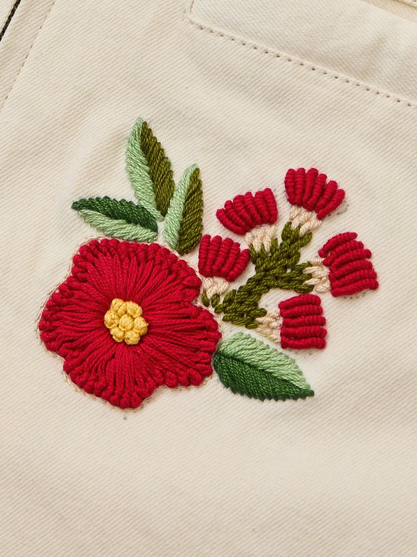 A red and yellow flower with green leaves, beautifully hand embroidered on beige fabric, decorates the Floral Hand Embroidered Work Jacket by Found.