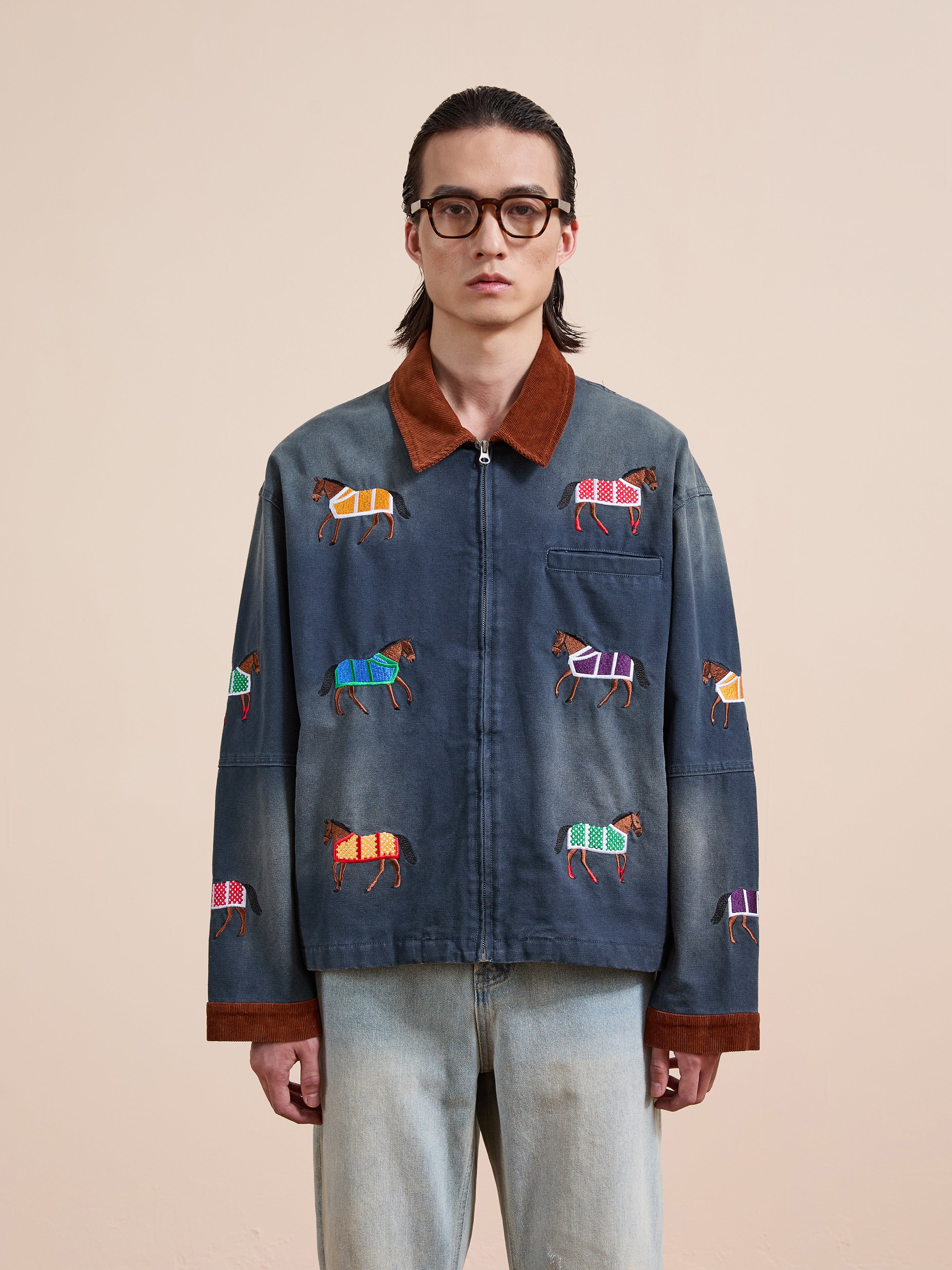 A person wearing glasses and the Found Lariat Horse Embroidered Work Jacket stands against a plain beige background.