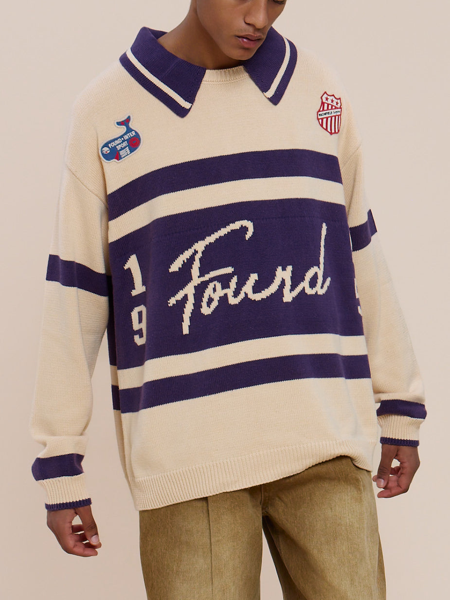 Person wearing the FOUND Knit Jersey in beige and purple with sports-inspired patches, paired with khaki pants against a plain light background.