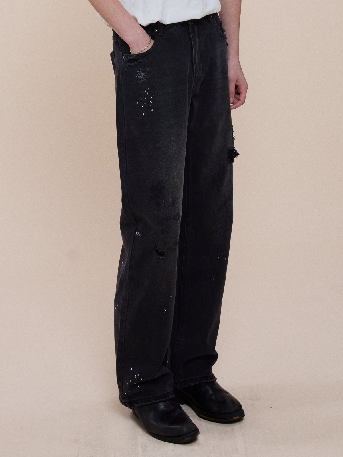 Person wearing FOUND Monet Paint Jeans, white t-shirt, and black shoes stands against a plain beige background with one hand in their pocket.