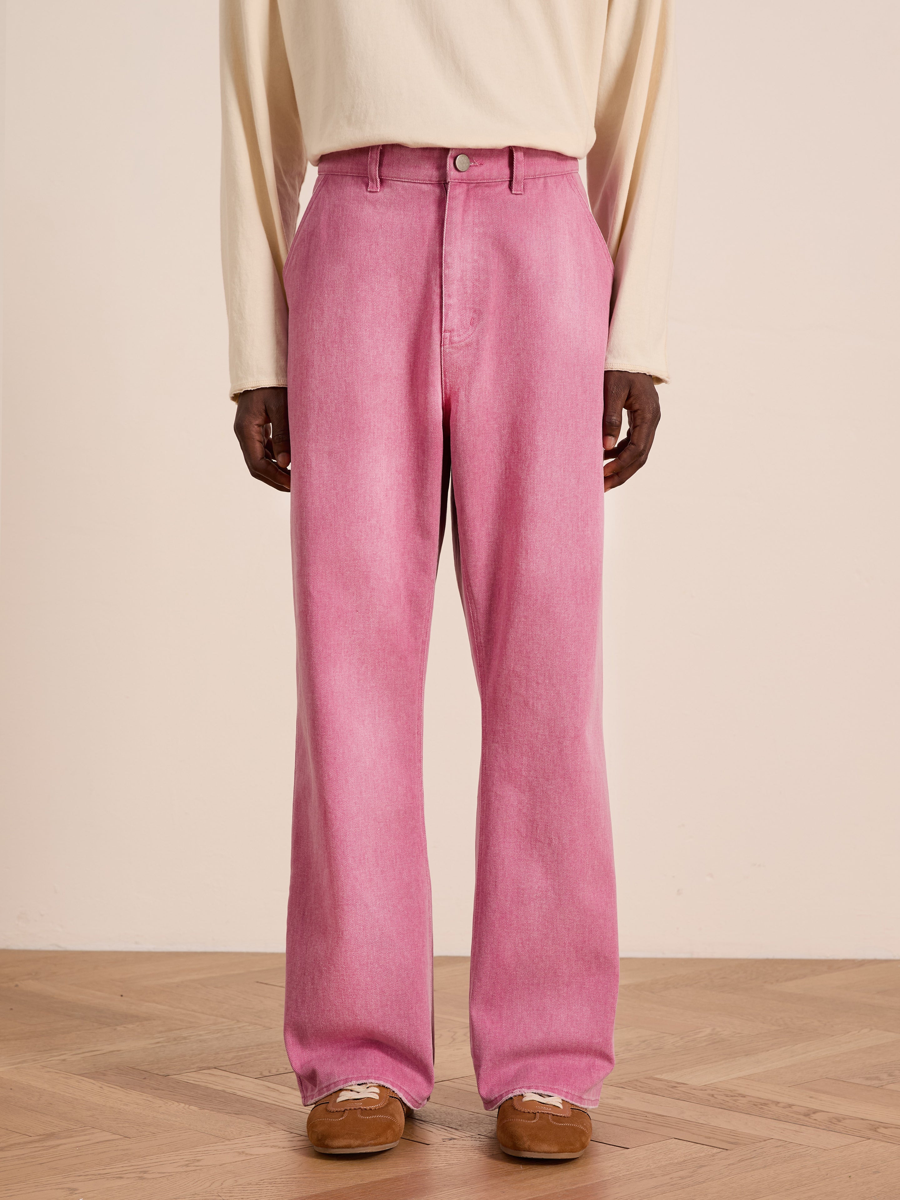 Person wearing FOUND Flare Work Pants in pink, a cream long-sleeve shirt, and brown suede shoes, standing on a wooden floor against a plain light background.