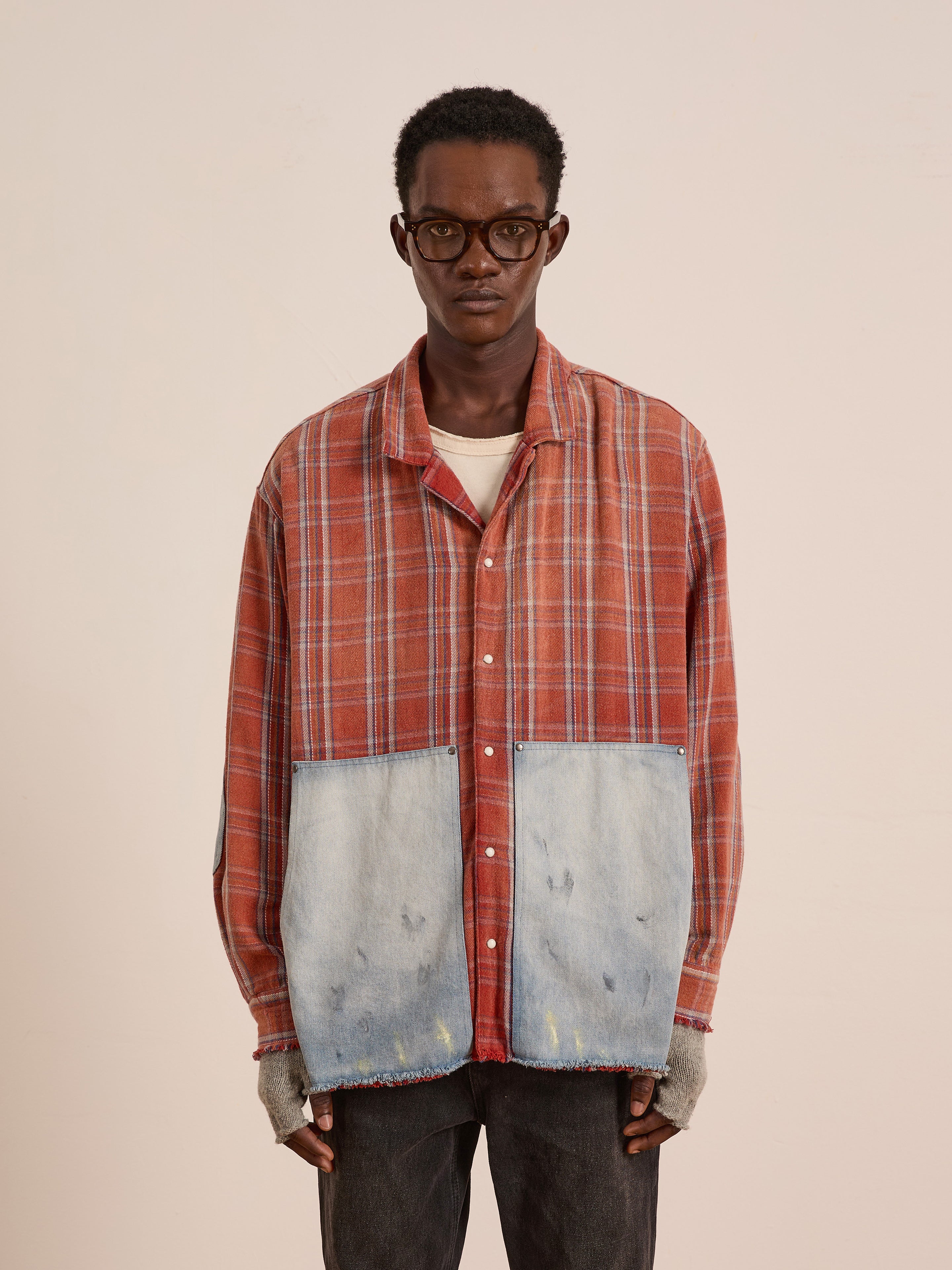 A person wearing glasses, the FOUND Plaid Denim Shirt with large denim patch pockets, fingerless gloves, and black pants stands against a plain background.