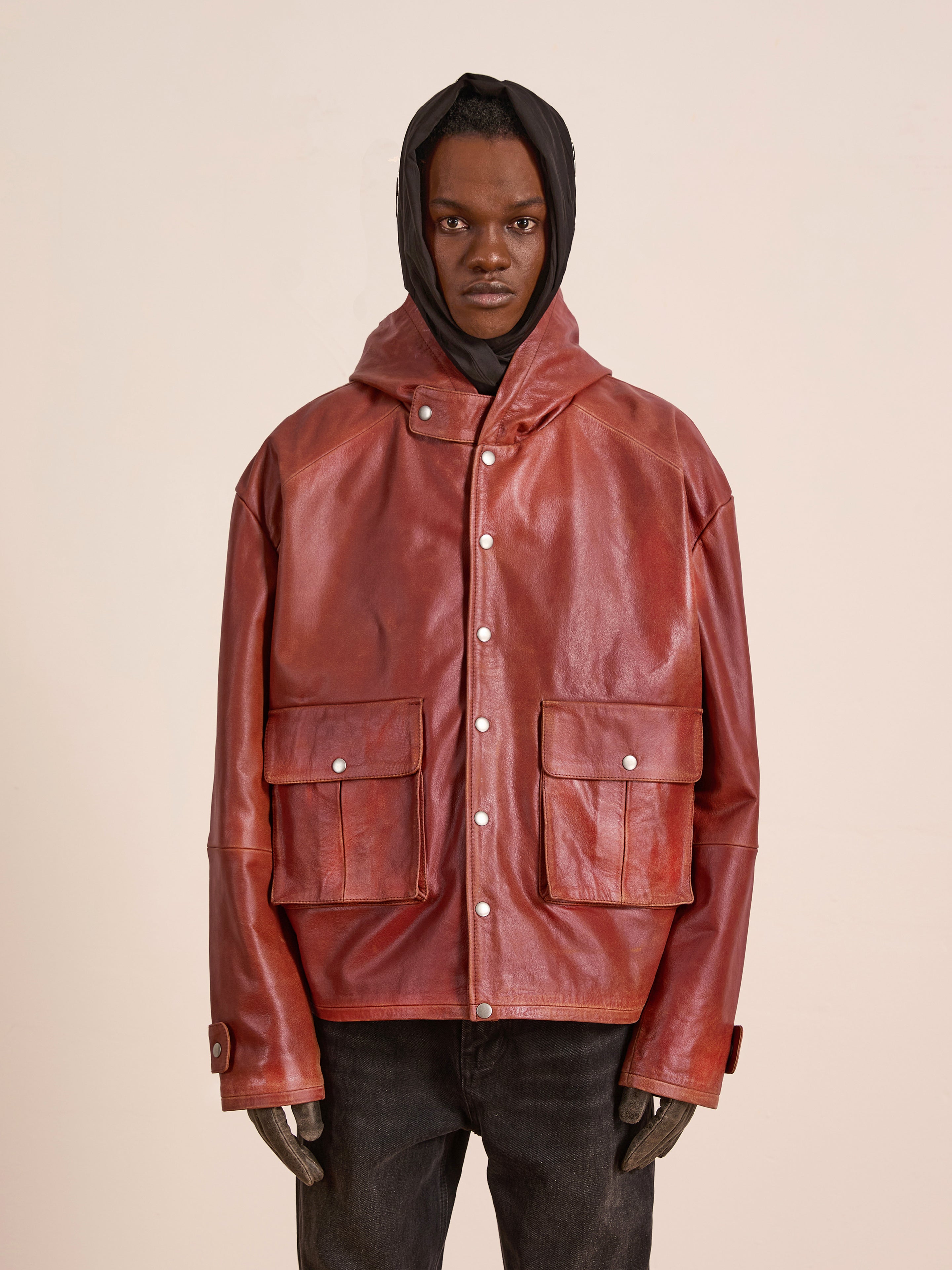 A person wears the FOUND Distressed Leather Pocket Hoodie, featuring a vintage red distressed leather look and large front pockets, standing facing forward against a plain light background.