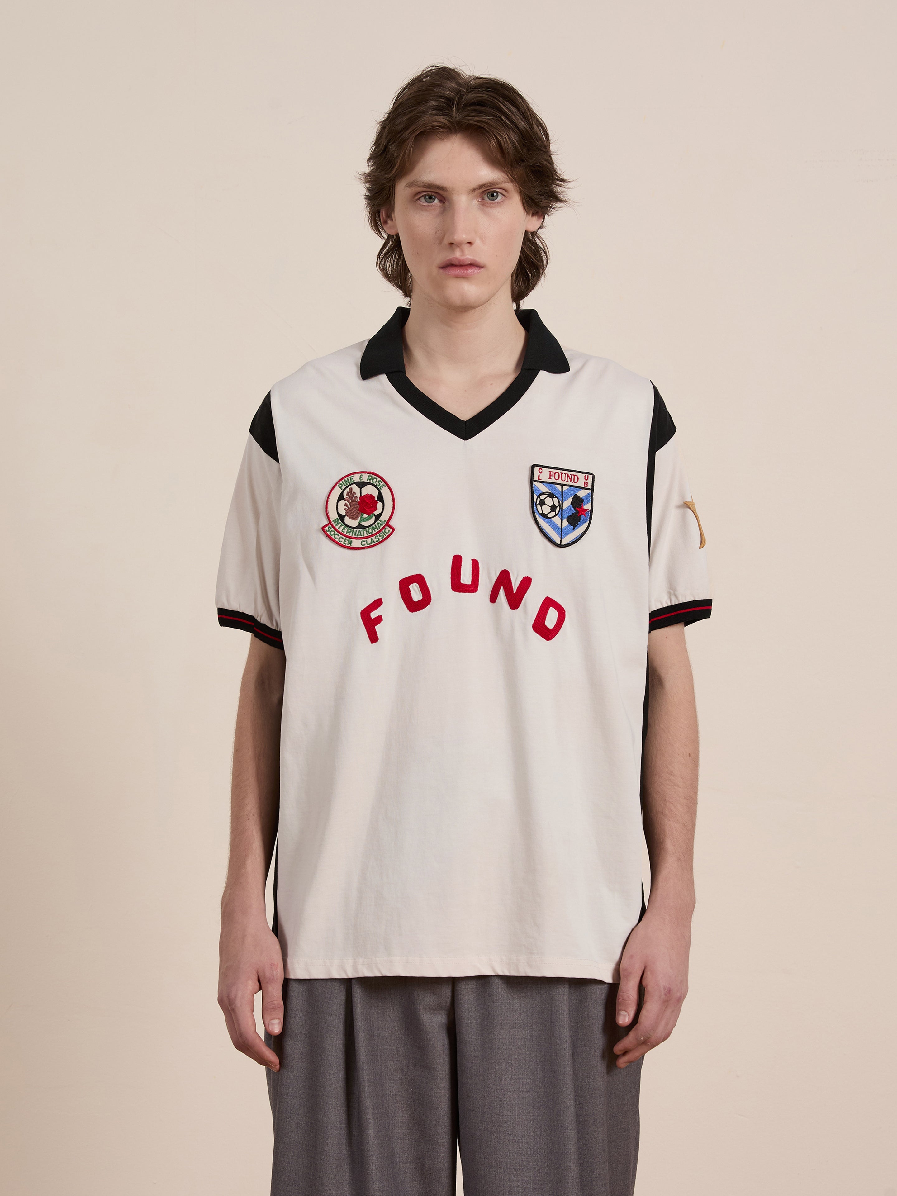 Clad in a sleek Union Soccer Jersey by FOUND, featuring bold "FOUND" text and badges, an individual stands against a plain backdrop, reminiscent of contemporary sportswear design.