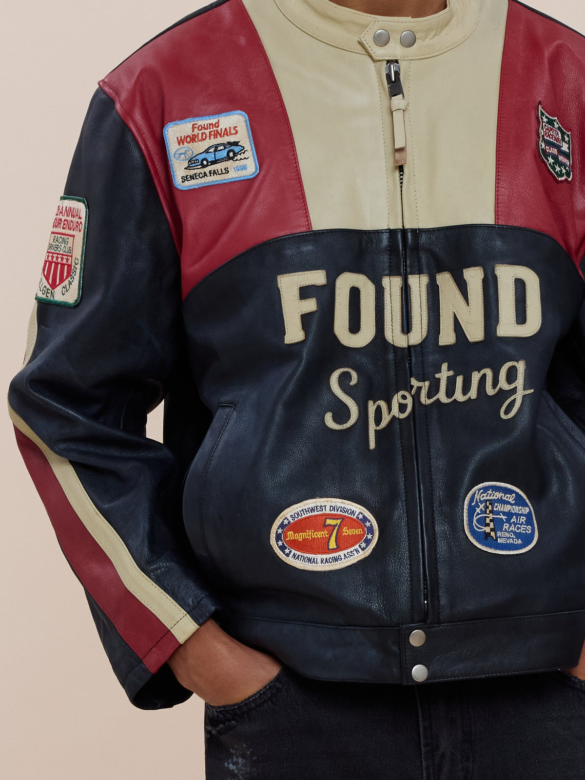 Person wearing the FOUND Sport Racer Jacket with color-blocked leather, racing patches, and “FOUND Sporting” on the front, standing hands in pockets.