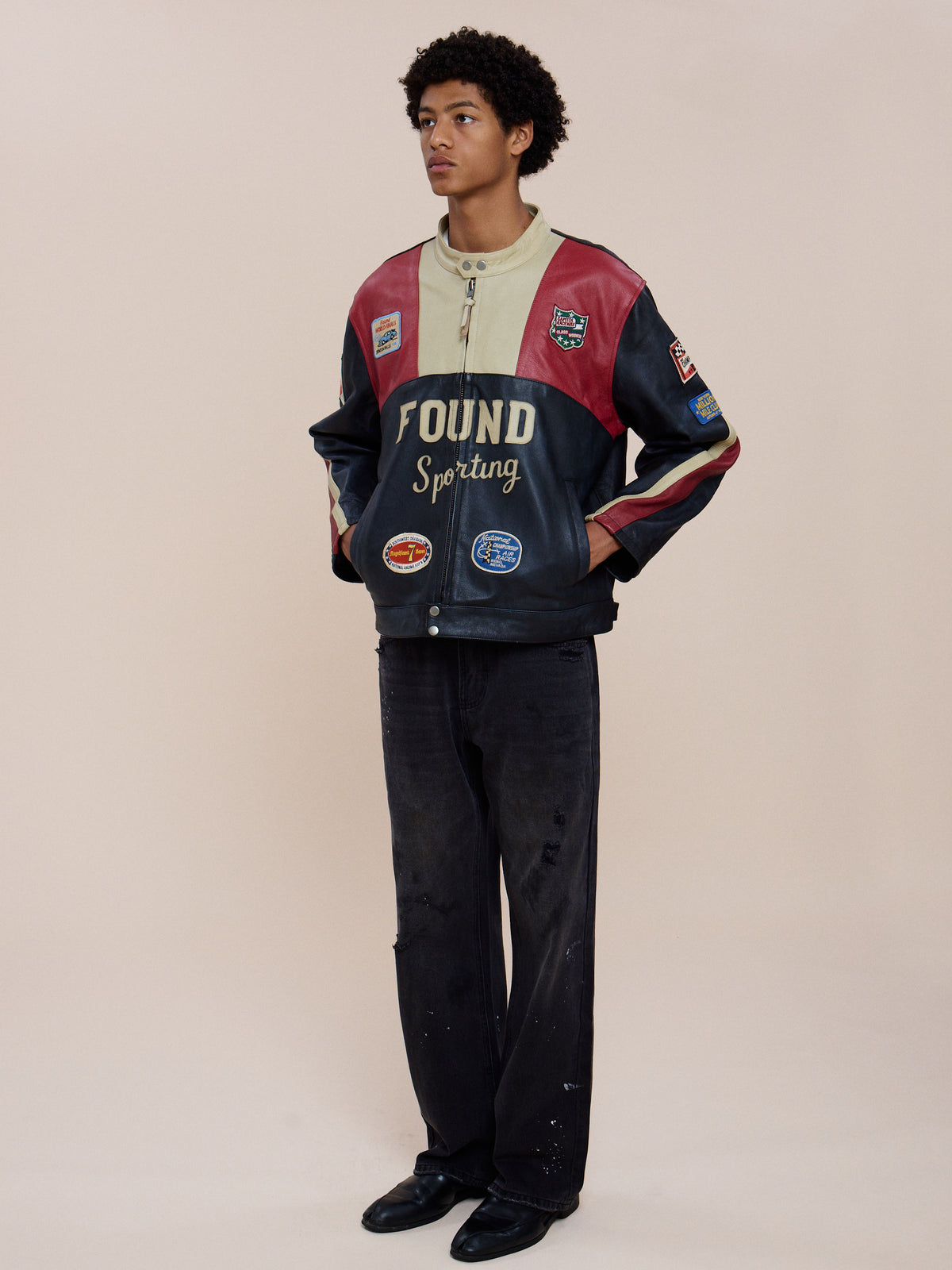 Person stands against a plain background in the FOUND Sport Racer Jacket, black pants, and black shoes, looking off to the side with hands in pockets.