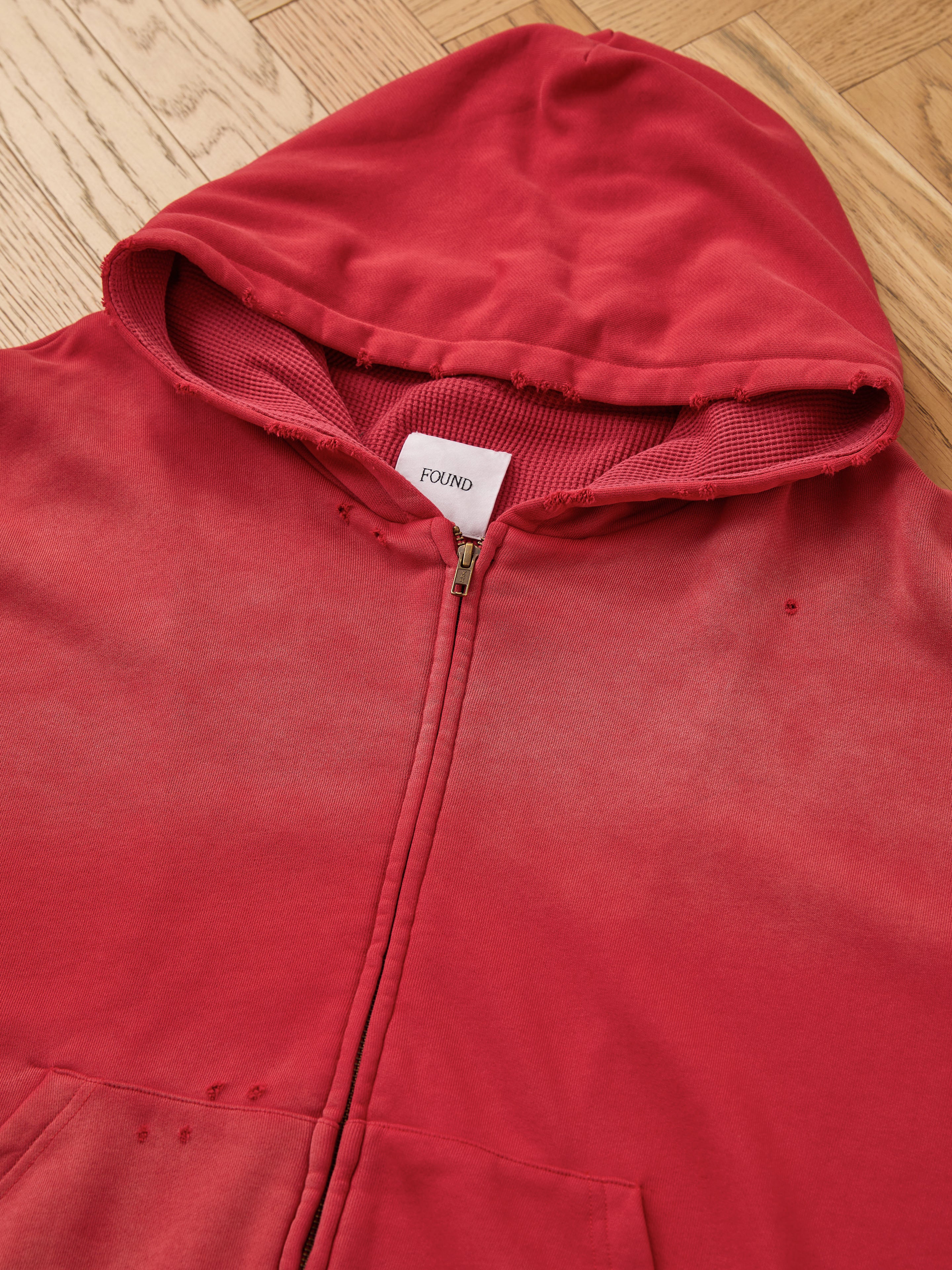 FOUND Distressed Thermal Lined Zip Up Hoodie in red, unisex relaxed fit, with visible small holes and light wear; shown laid flat on a wood floor.