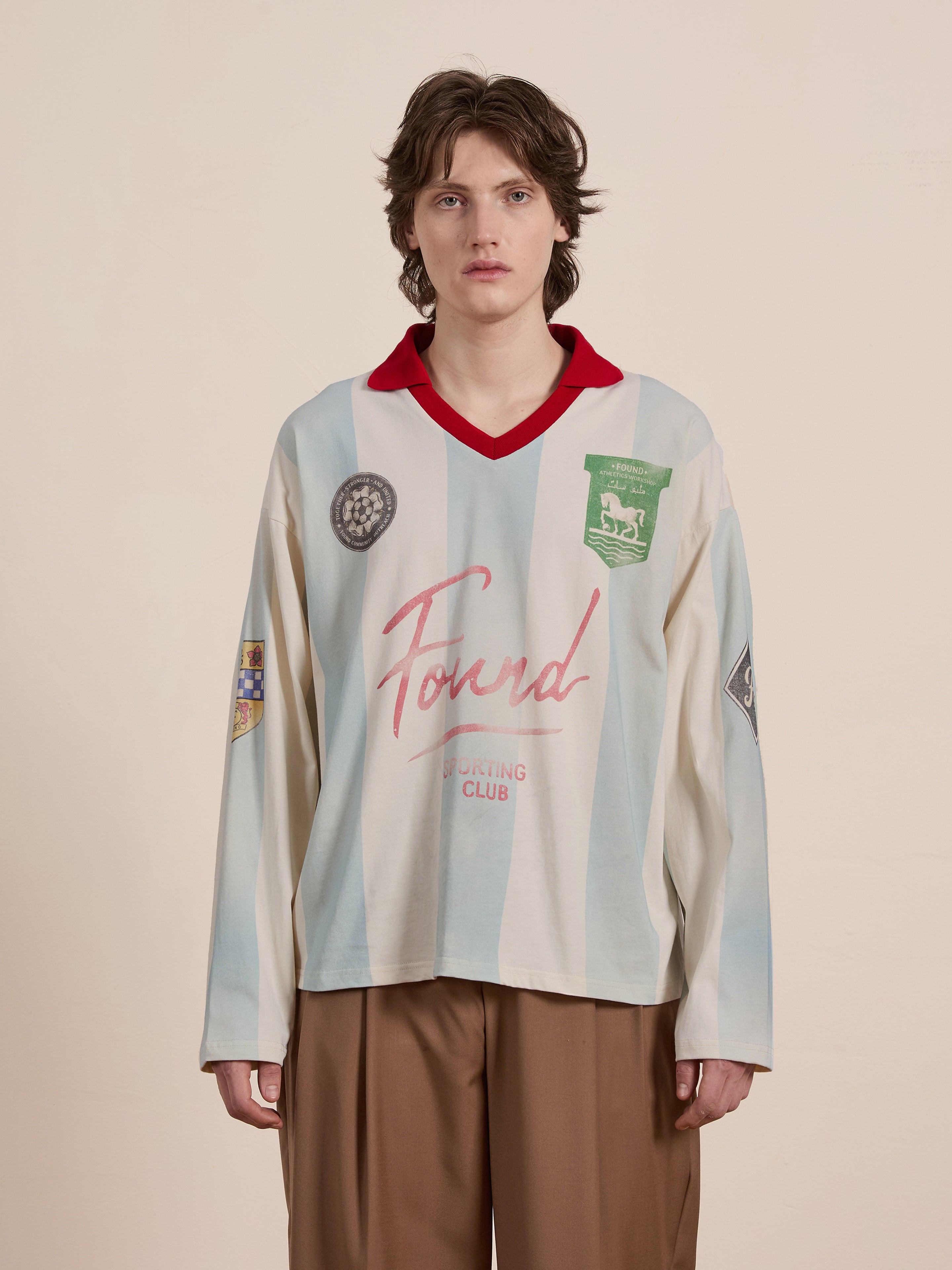 A person stands against a plain background wearing the FOUND Striped Sport LS Jersey paired with brown pants.