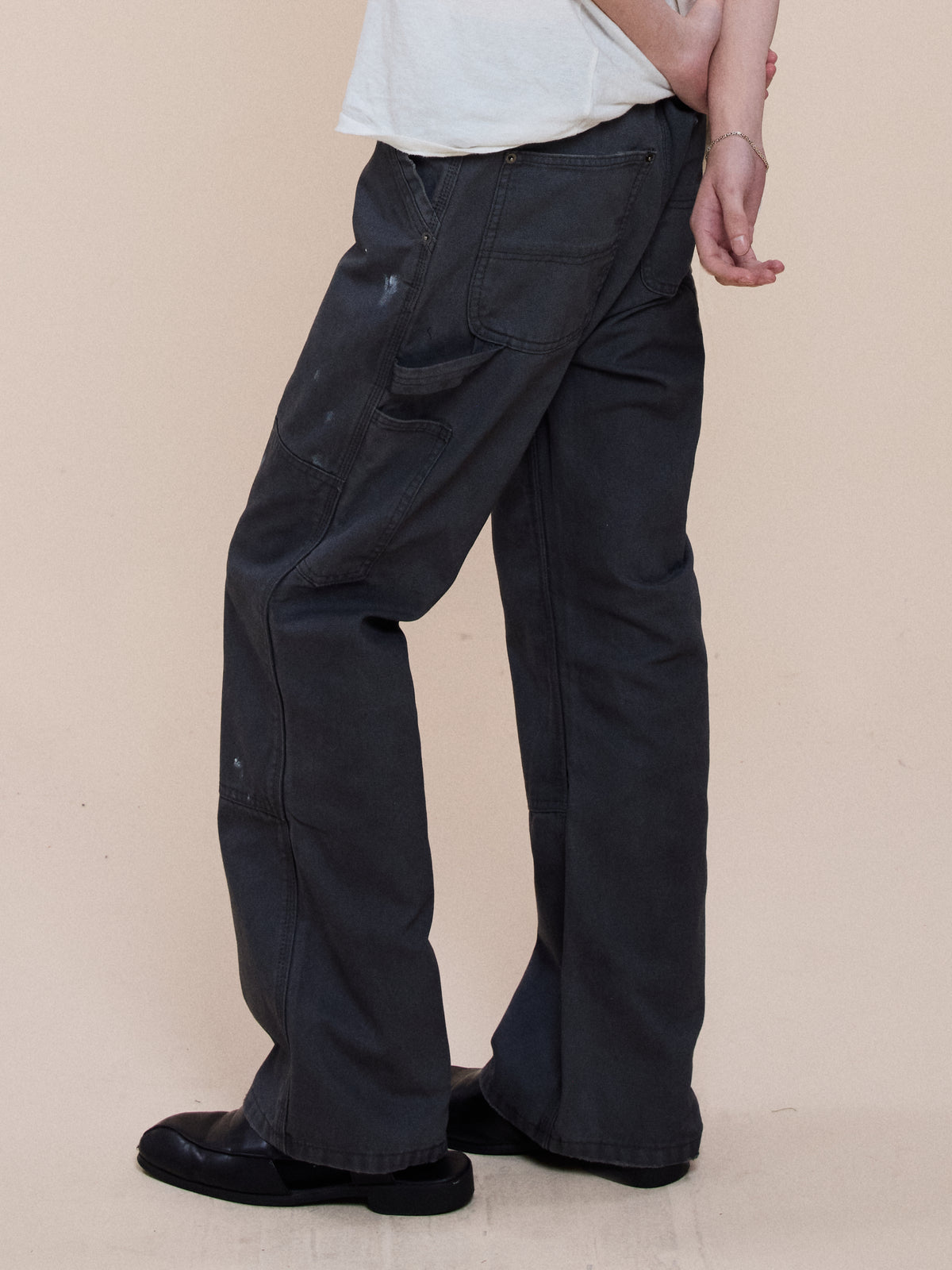 Person stands sideways in a white shirt, FOUND Sunbleached Utility Pants, and black shoes, one arm bent behind their back against a plain background.