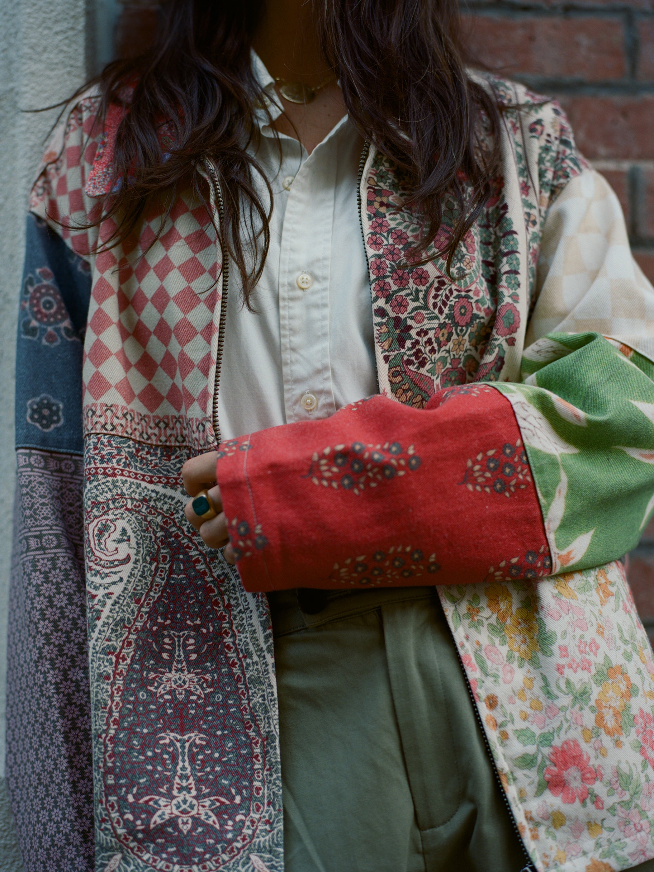 Wearing the FOUND Tapestry Twill Jacket with patchwork in various patterns and colors, including a striking red sleeve, perfectly complements a crisp white shirt underneath, exuding vintage charm for any gender.
