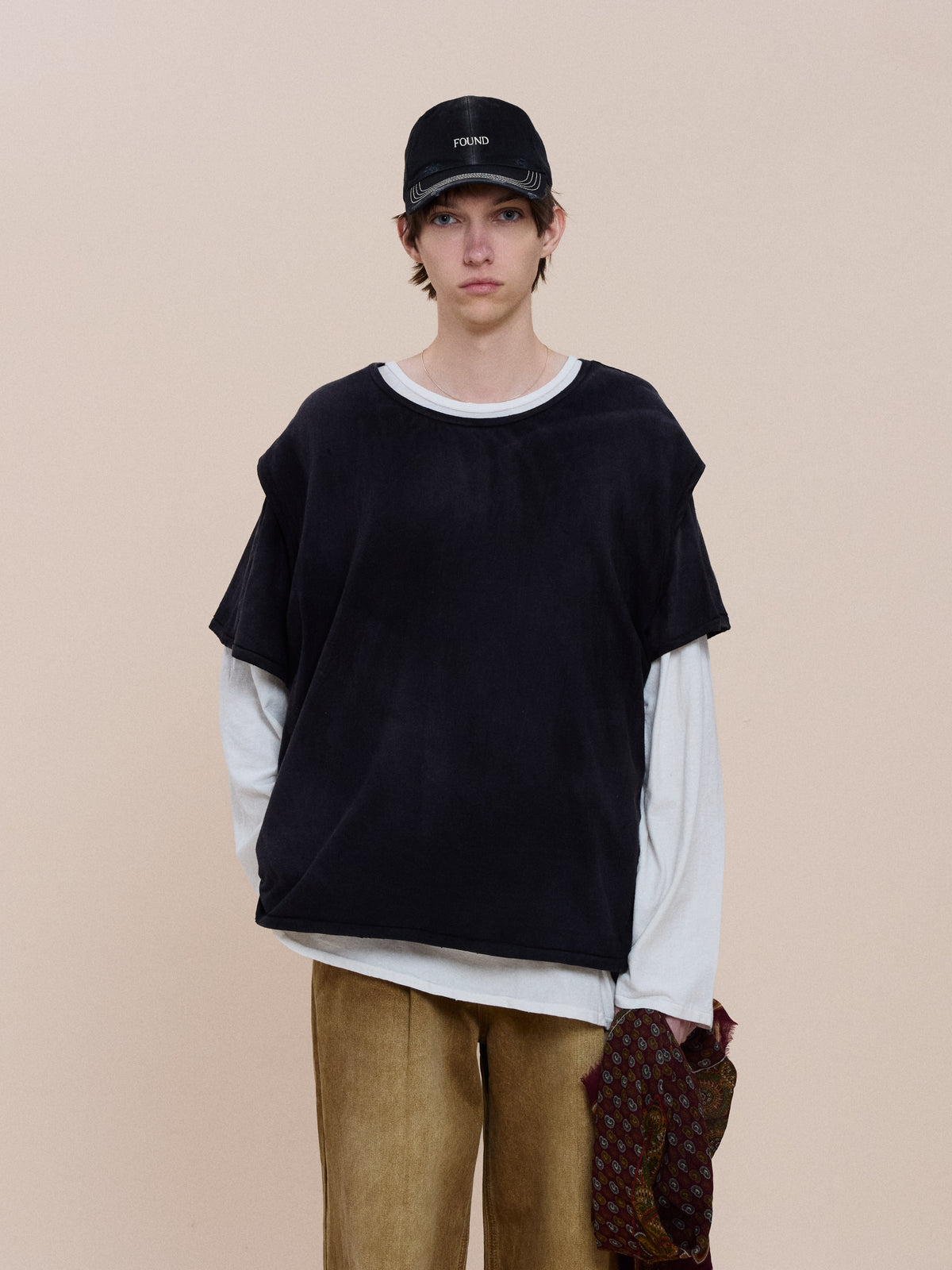 Model wears the Triple Layer Tee by FOUND, a relaxed fit oversized black shirt over a white long-sleeve top and tan pants, against a plain beige background.