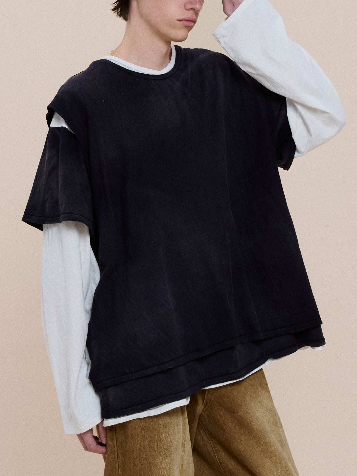 Model wears the Triple Layer Tee by FOUND, styled over a long-sleeve white shirt and tan pants, standing against a plain background.