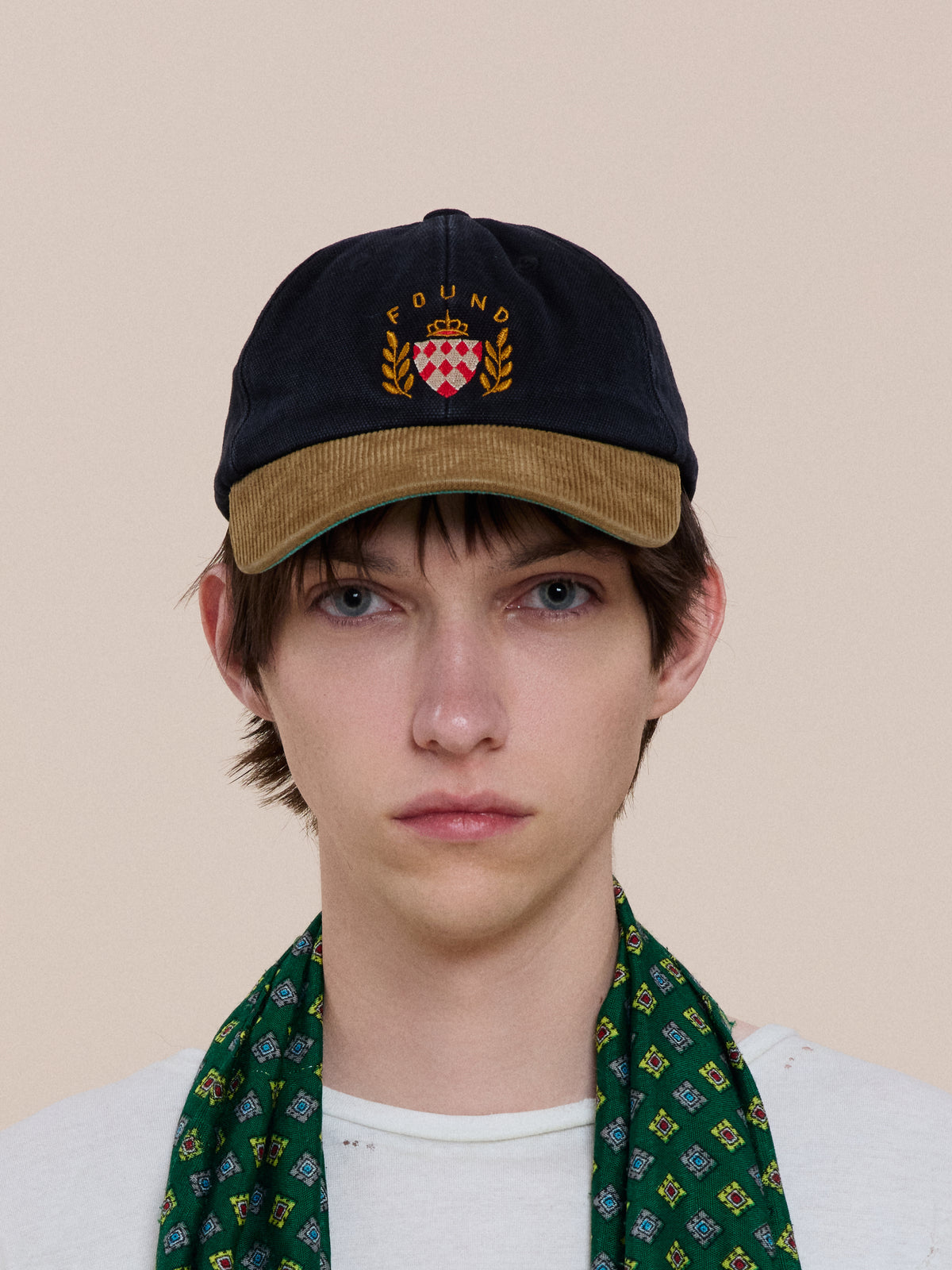 A person wears the Vintage Club Cap by Found, paired with a white shirt and green patterned scarf—heritage sportswear style on a light background.