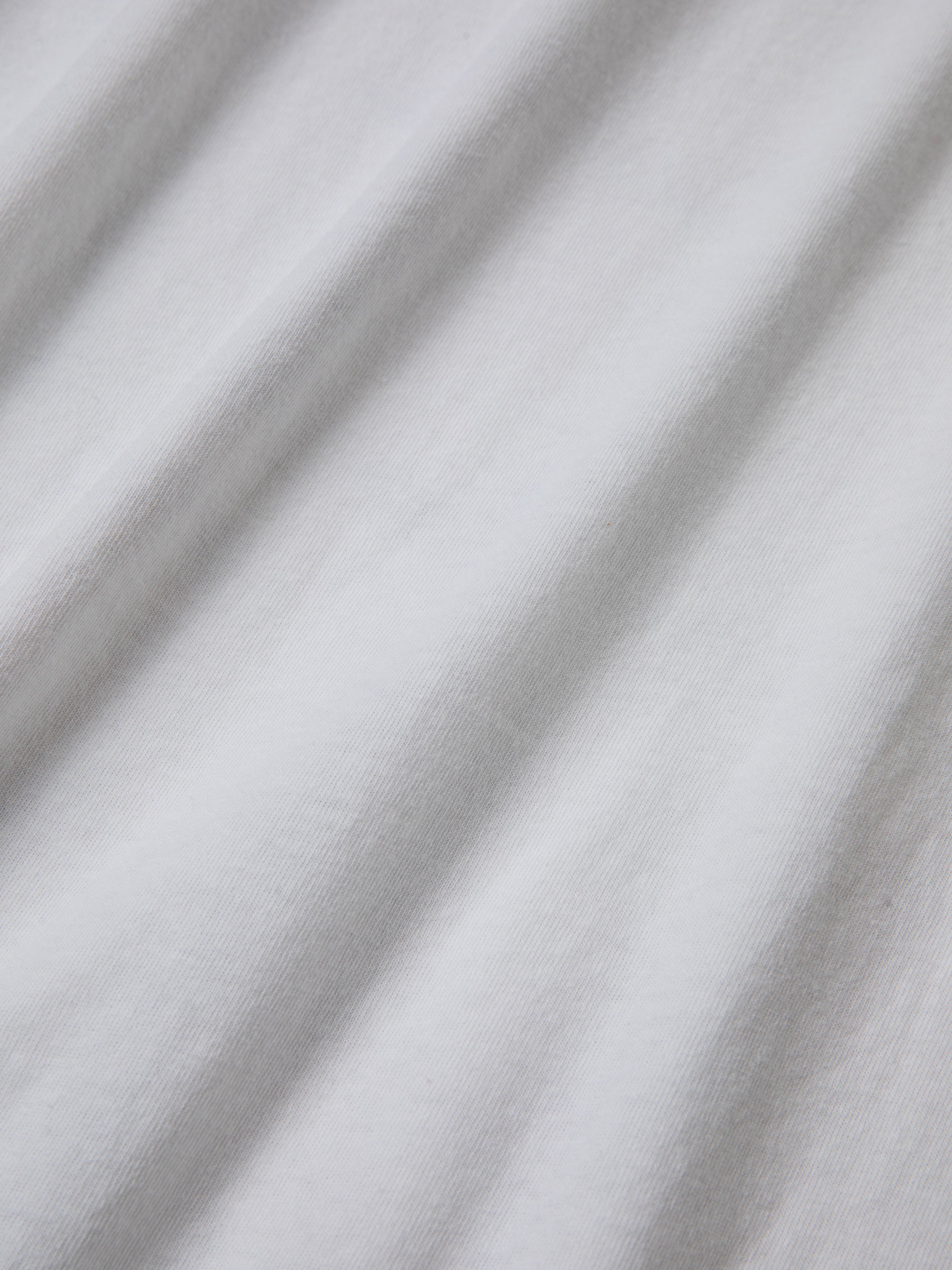 Close-up of white 100% cotton fabric with visible texture and subtle shadowing from folds, reminiscent of the classic Malibu Farm Fair Tee by FOUND.
