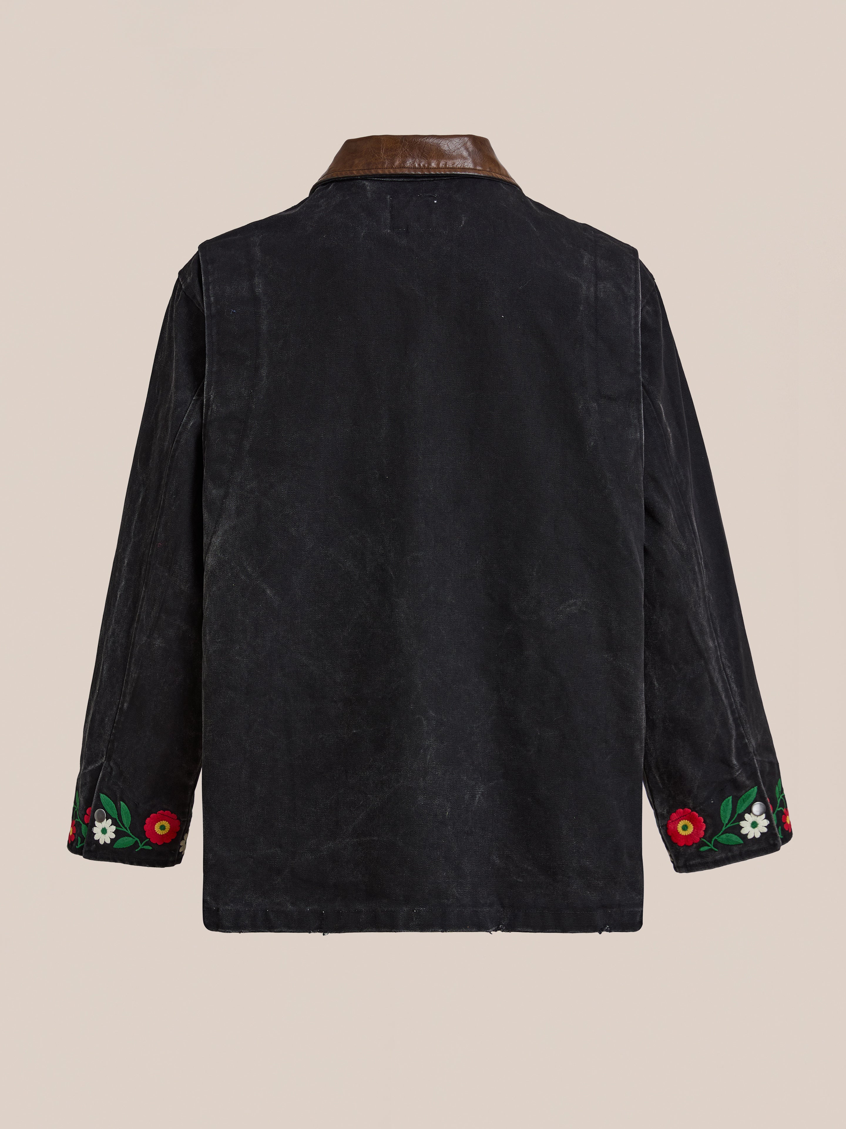 The Found Canvas Embroidered Work Jacket features a black canvas body, brown collar, subtle leather trim, and floral embroidery in red, white, and green on the cuffs; shown from the back.