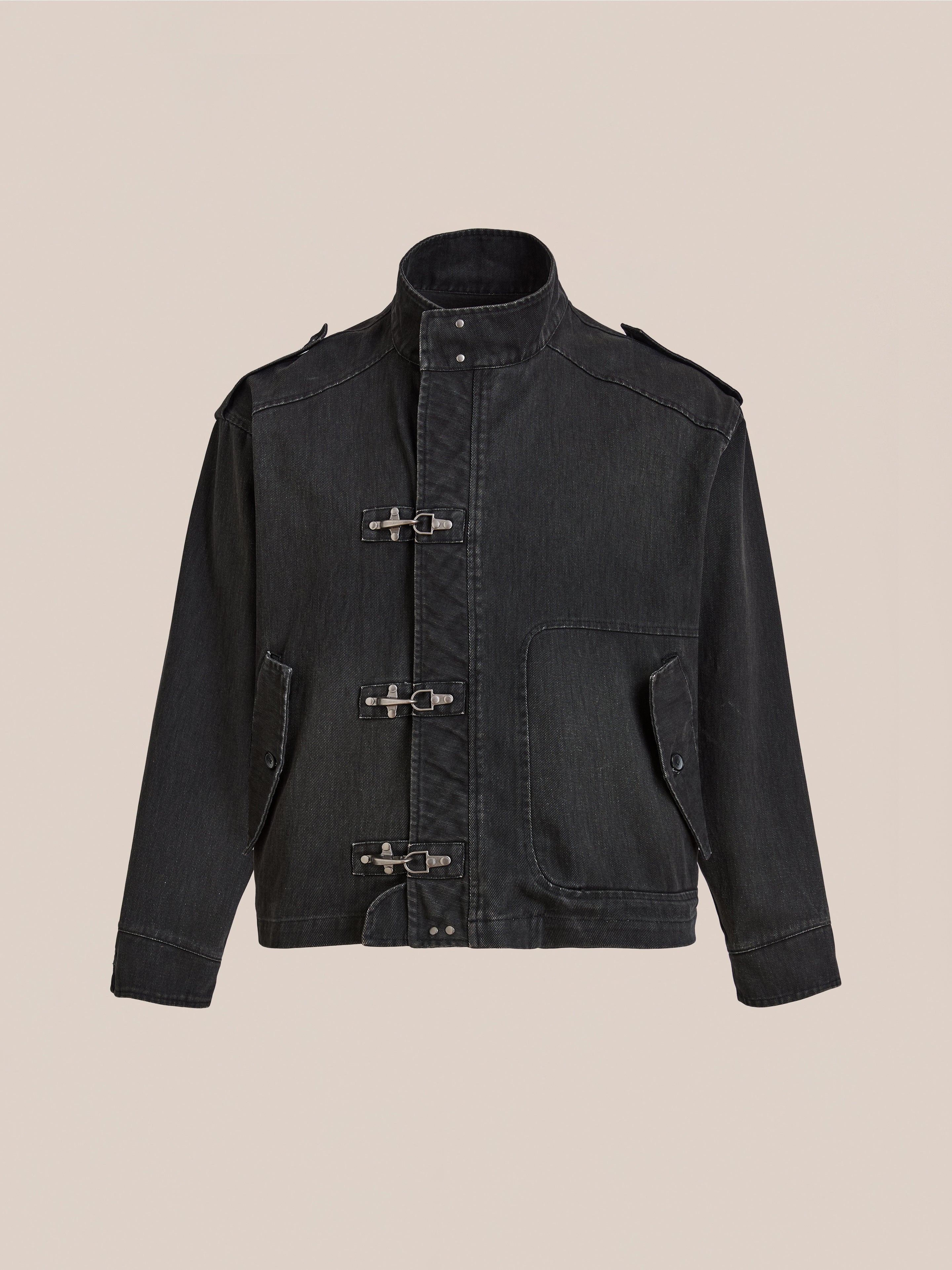 The Found Utility Clasp Work Jacket is a vintage black cotton style with a high collar, three fireman clasps, two front flap pockets, and shoulder epaulets, shown against a light beige background.