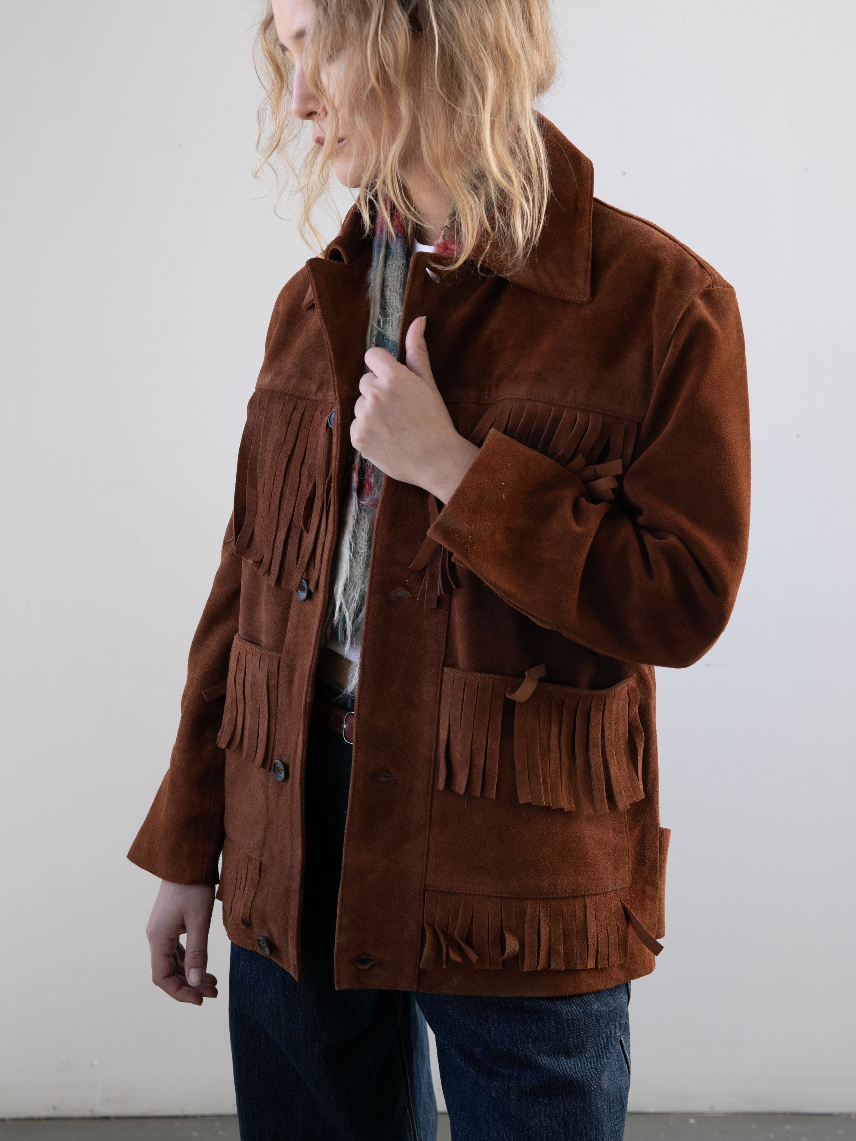 A person models the FOUND Western Suede Fringe Jacket over a patterned shirt and blue jeans, standing against a plain light background.