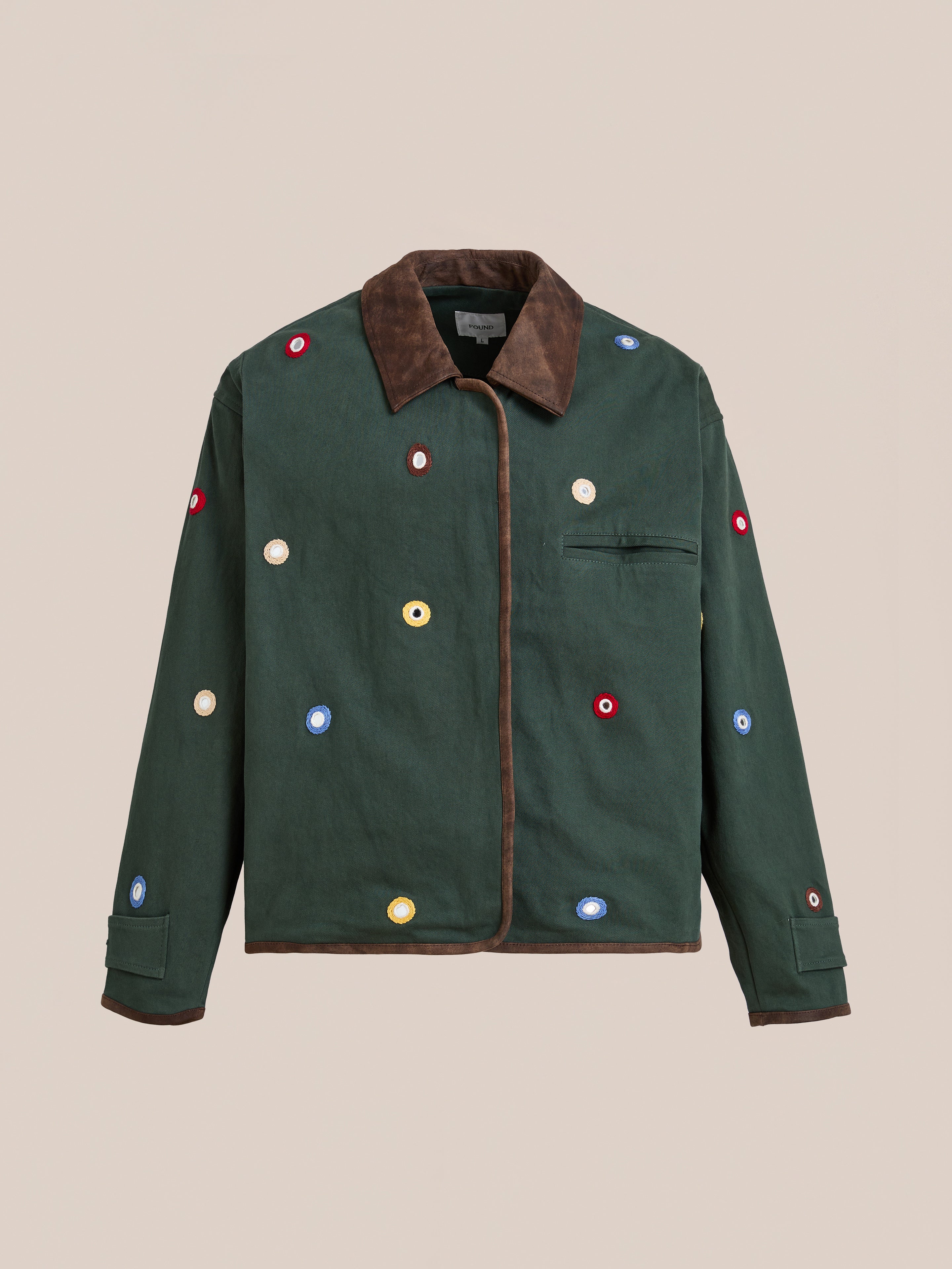 The Found Hand Embroidered Mirror Abhala Jacket is a handcrafted cotton twill jacket in dark green with a brown collar and trim, scattered colorful circular appliqués, and a single visible chest pocket.