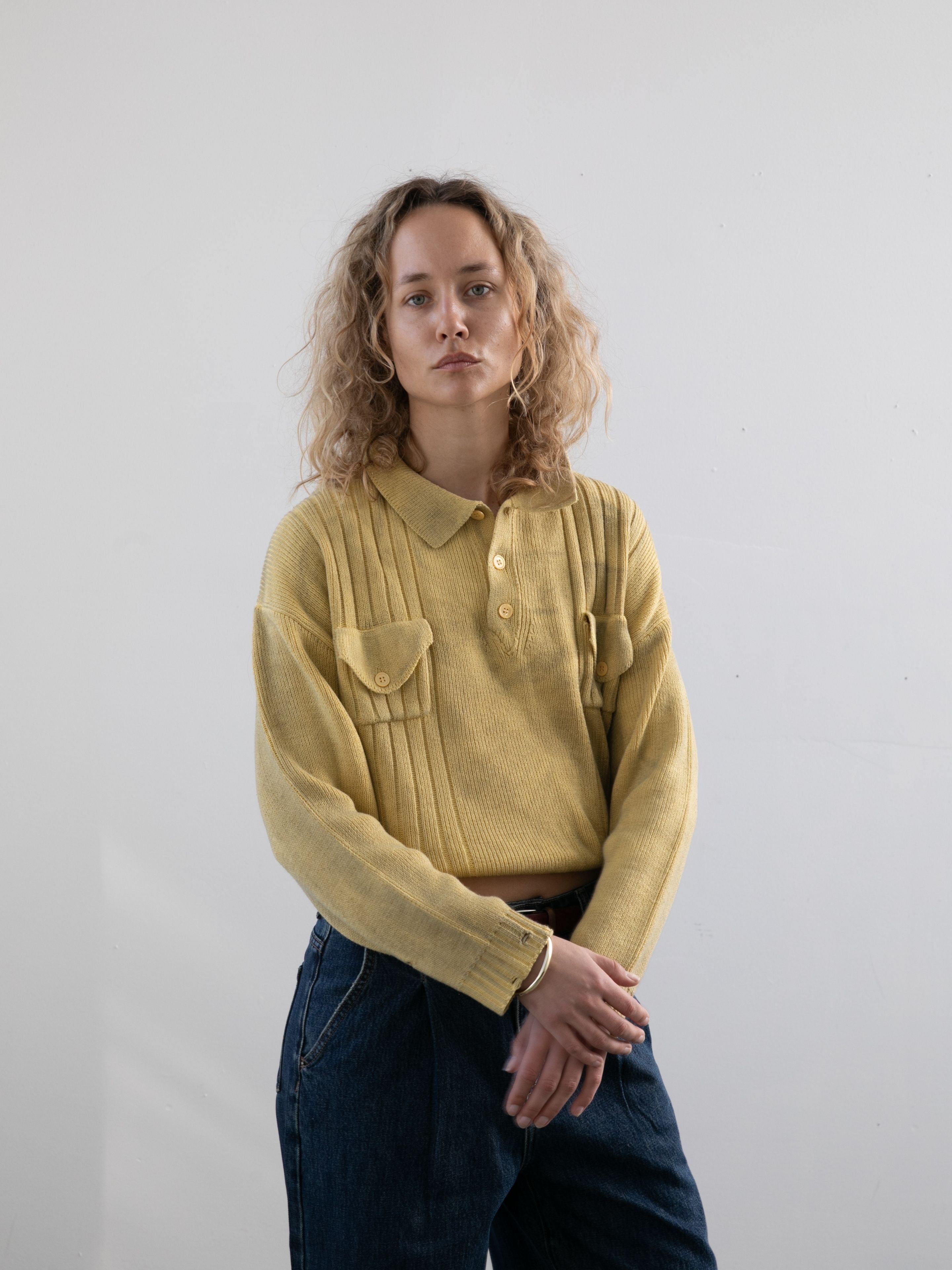 A person with curly hair wears the FOUND Distressed Pullover Knit and blue jeans, standing against a plain white background and looking directly at the camera with a neutral expression.