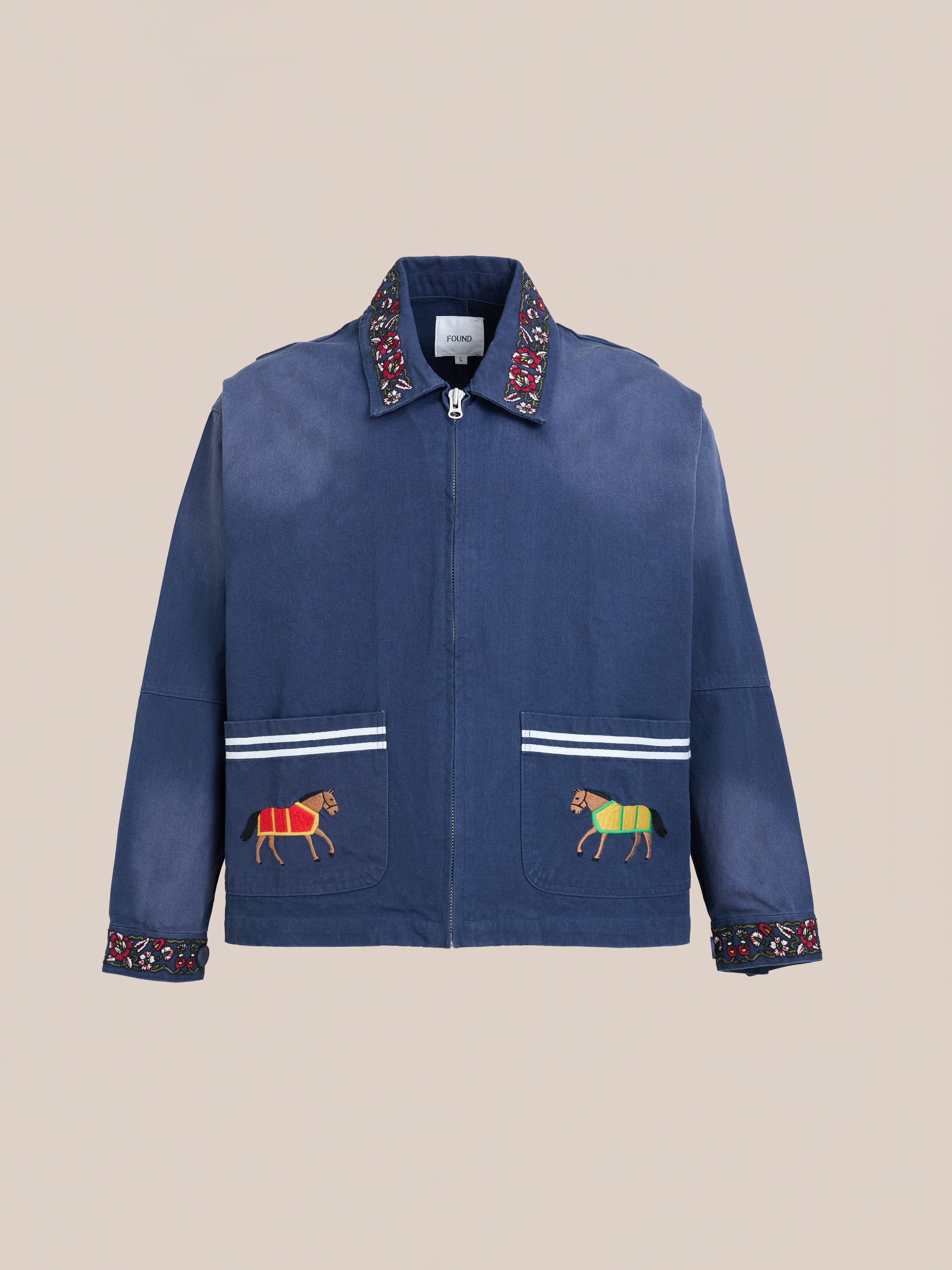 The Found Horse Equine Work Jacket is a blue jacket with embroidered patterns on the collar and cuffs, plus two front pockets each featuring an embroidered animal motif, inspired by traditional racing colours.
