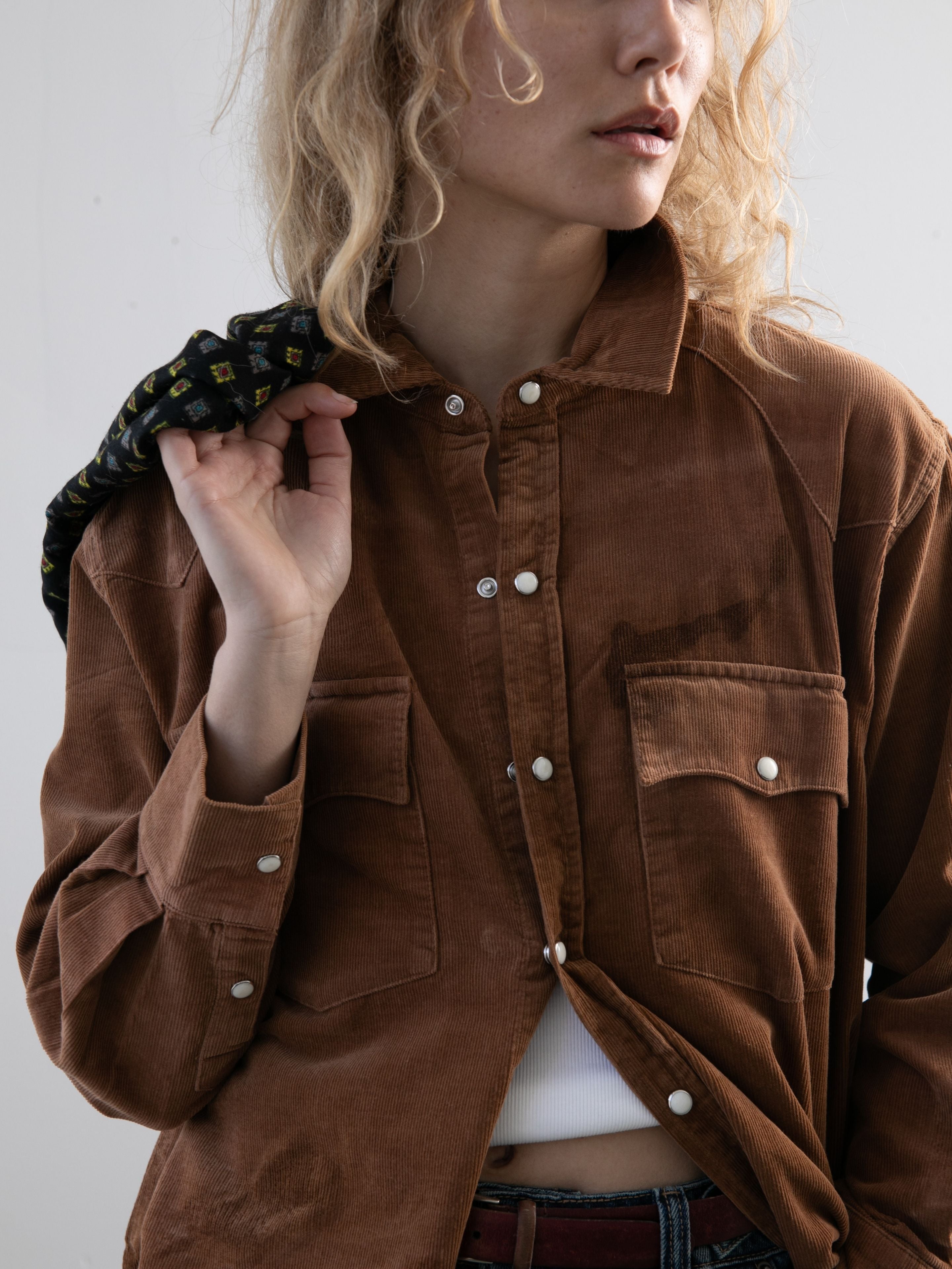 A person wears the FOUND Western Corduroy Shirt over a white top, holding a patterned jacket over their shoulder against a plain background.