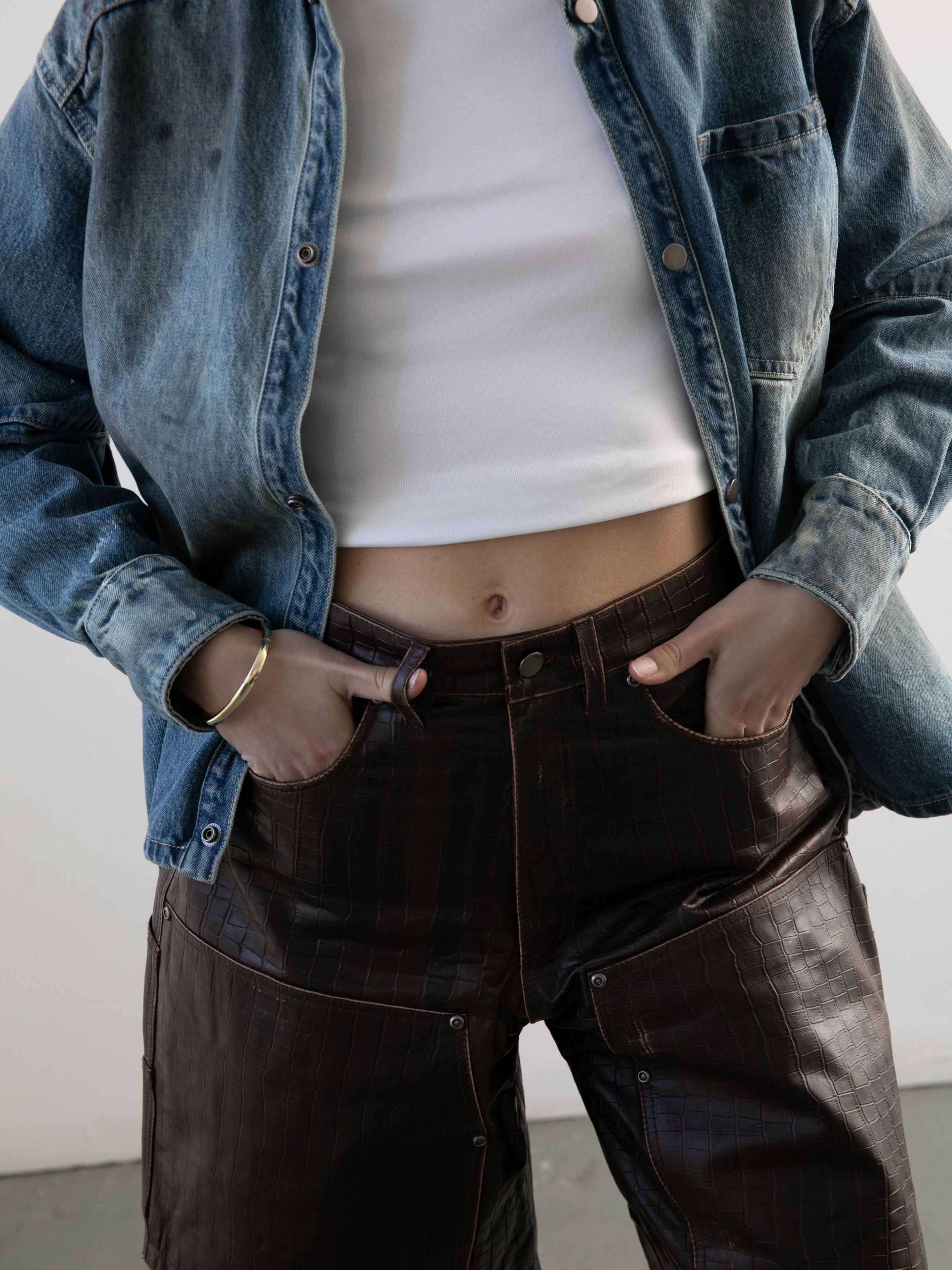 Model wears FOUND Distressed Croc Embossed Leather Shorts with hands in pockets, styled with a white crop top and blue denim jacket, shown from shoulders to thighs.