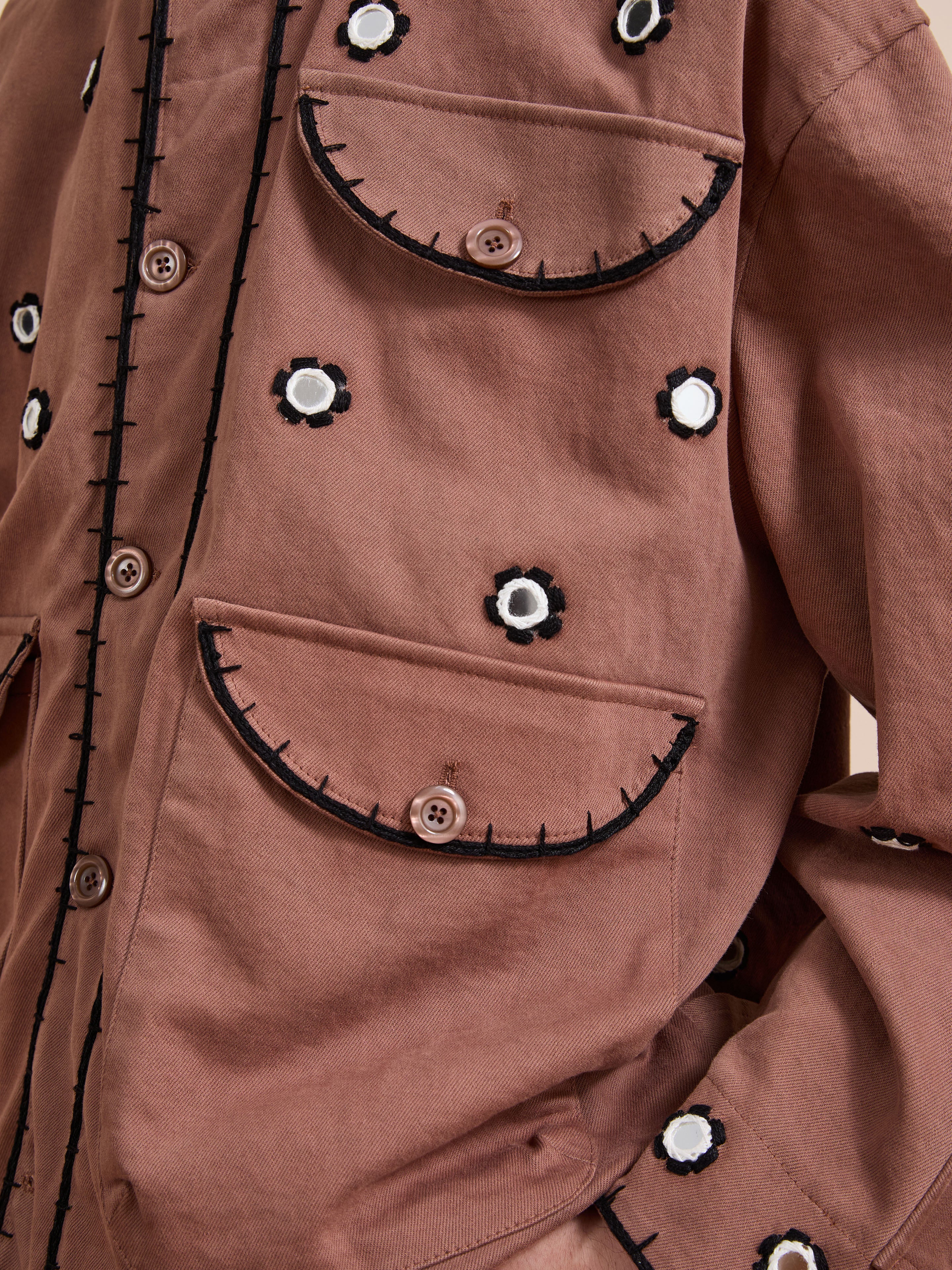 Close-up of the FOUND Hand Embroidered Hooded Mirror Anorak in brown cotton twill, featuring two front pockets, black and white Sheesha Kari floral mirror embroidery, and button closures.