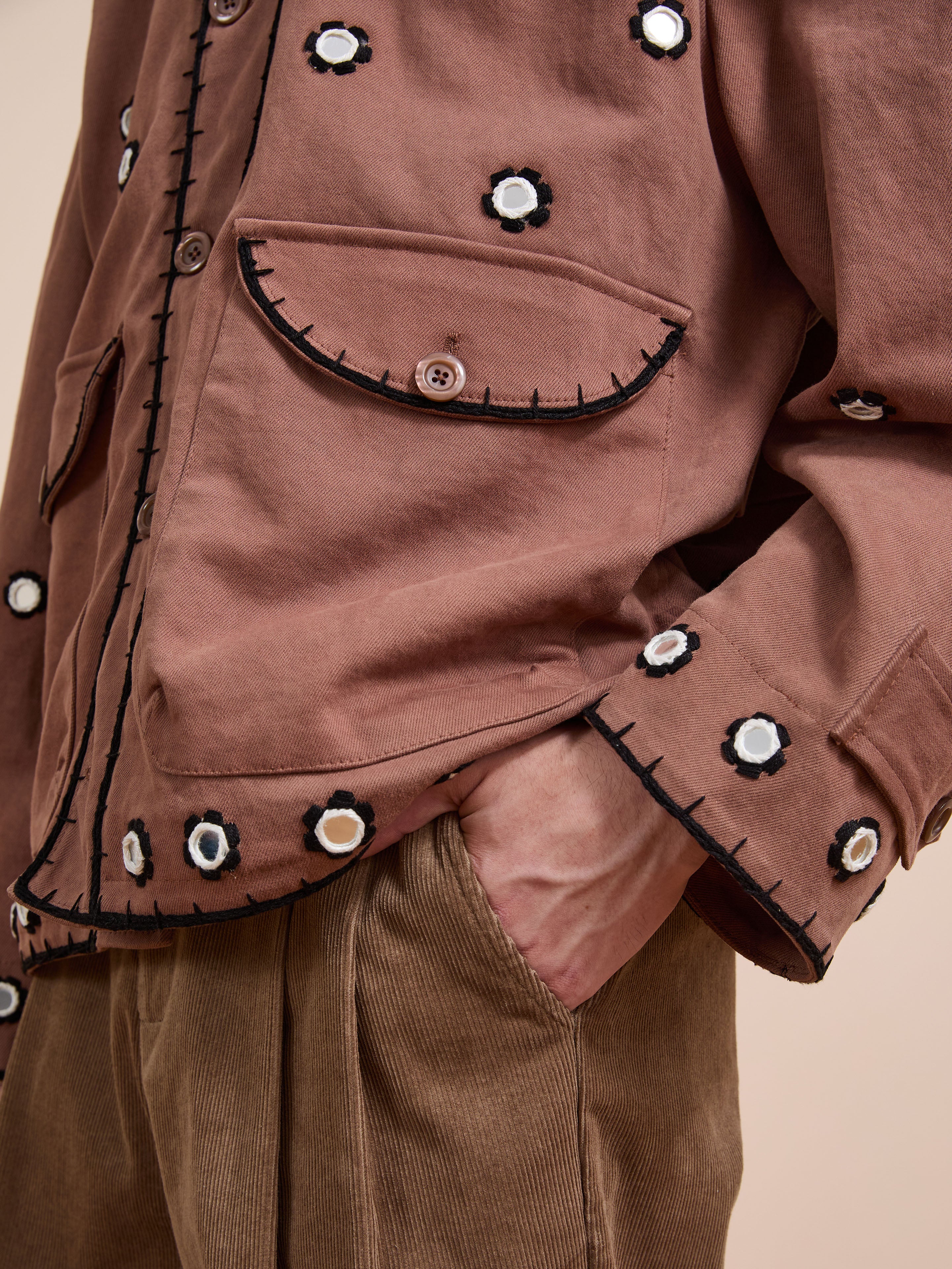 A person wears the FOUND Hand Embroidered Hooded Mirror Anorak with black and white floral mirror embroidery and brown corduroy pants, with their left hand in their pocket.