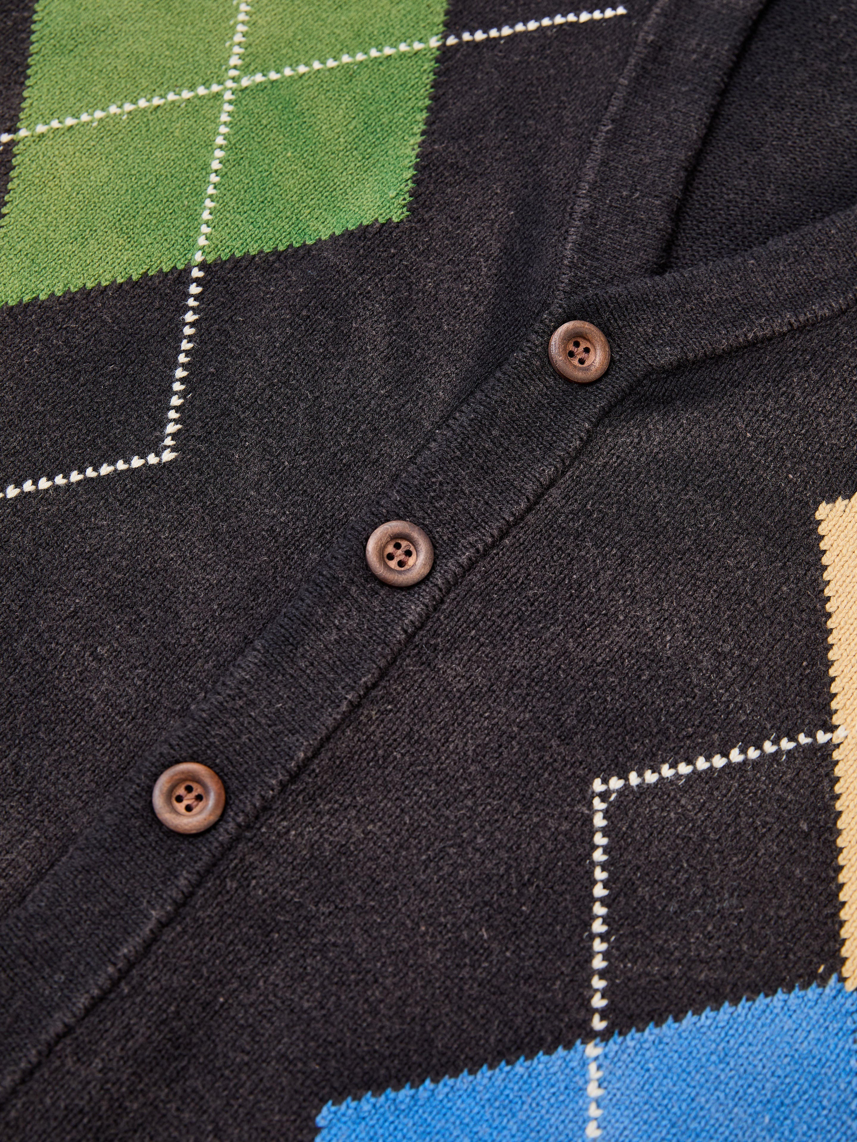 Close-up of the FOUND Argyle Knit Cardigan, an oversized black knit with brown buttons and a vibrant green, yellow, and blue argyle pattern.