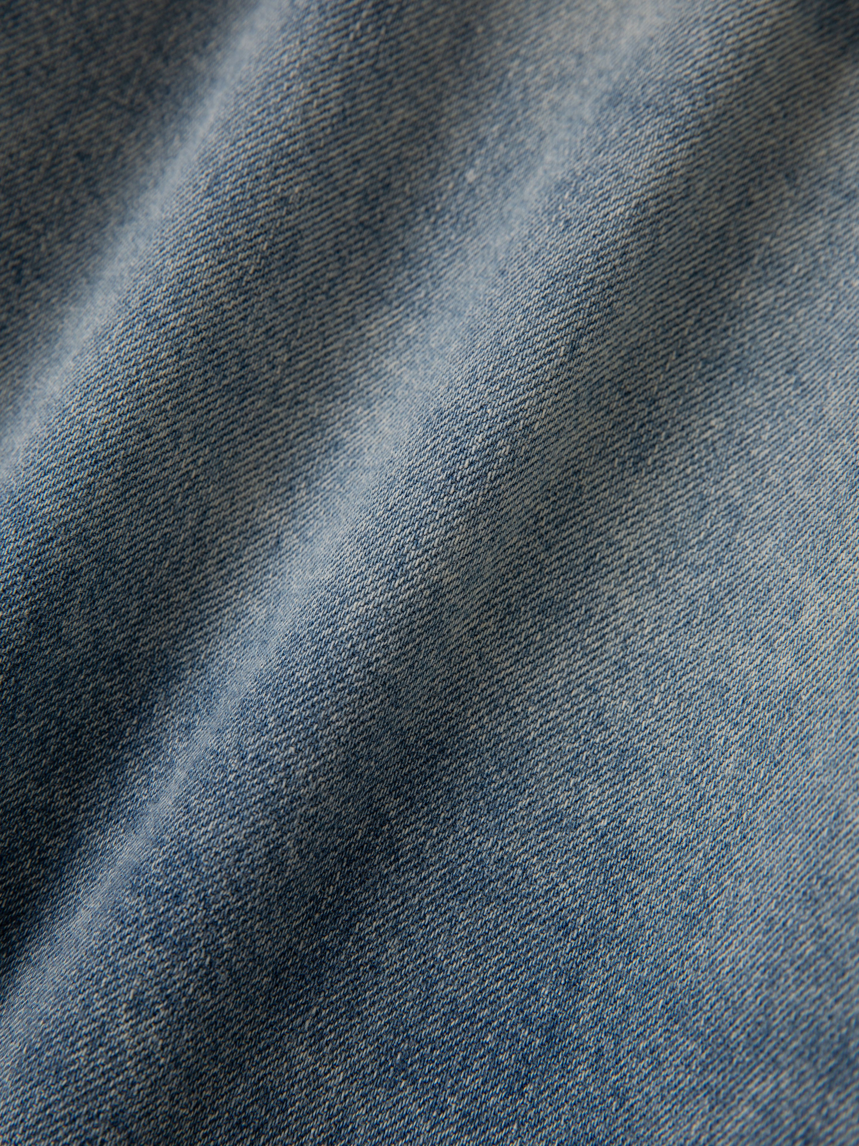 Close-up of blue denim fabric on the FOUND Bouquet Floral Embroidered Western Denim Shirt, showcasing its detailed texture and soft diagonal folds.