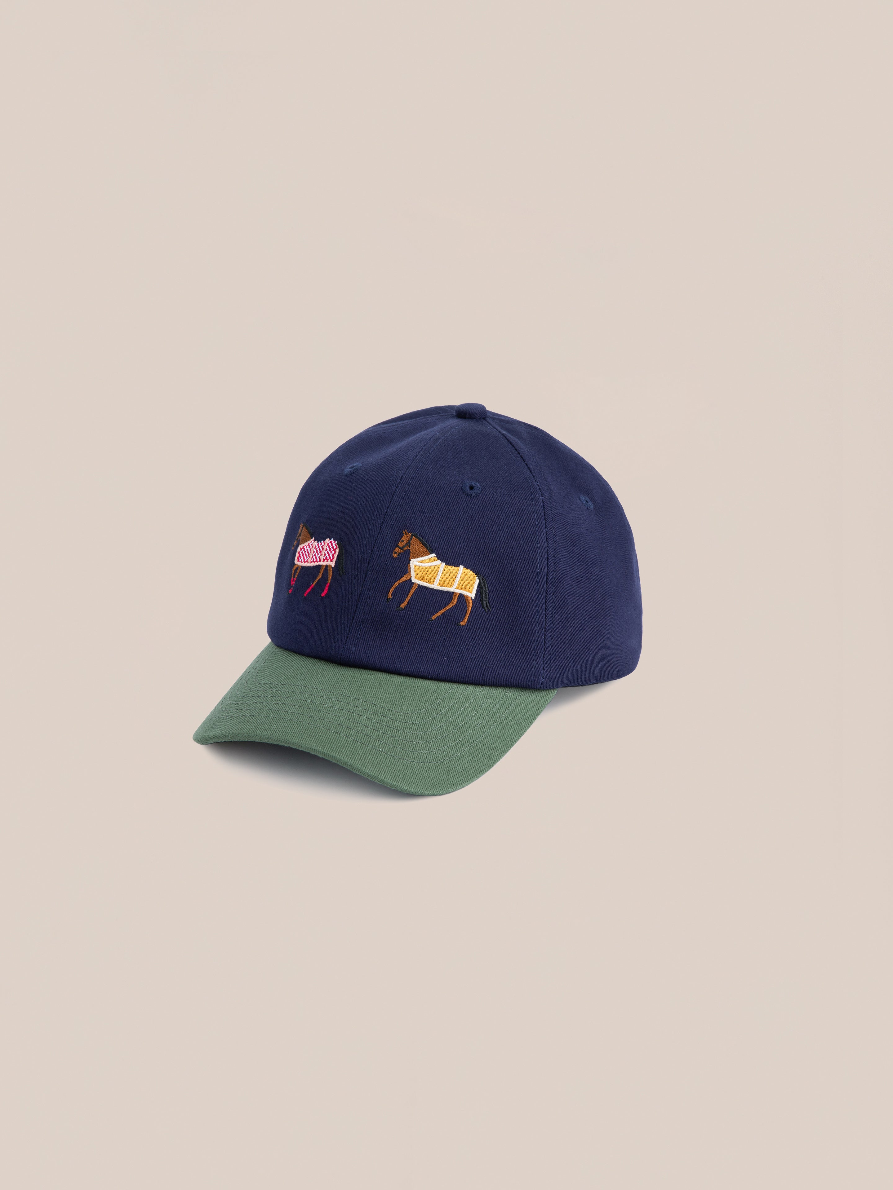 The Found Horse Equine Cap combines navy blue with a green brim, featuring embroidered designs of two horses on the front, adding a touch of racing flair.