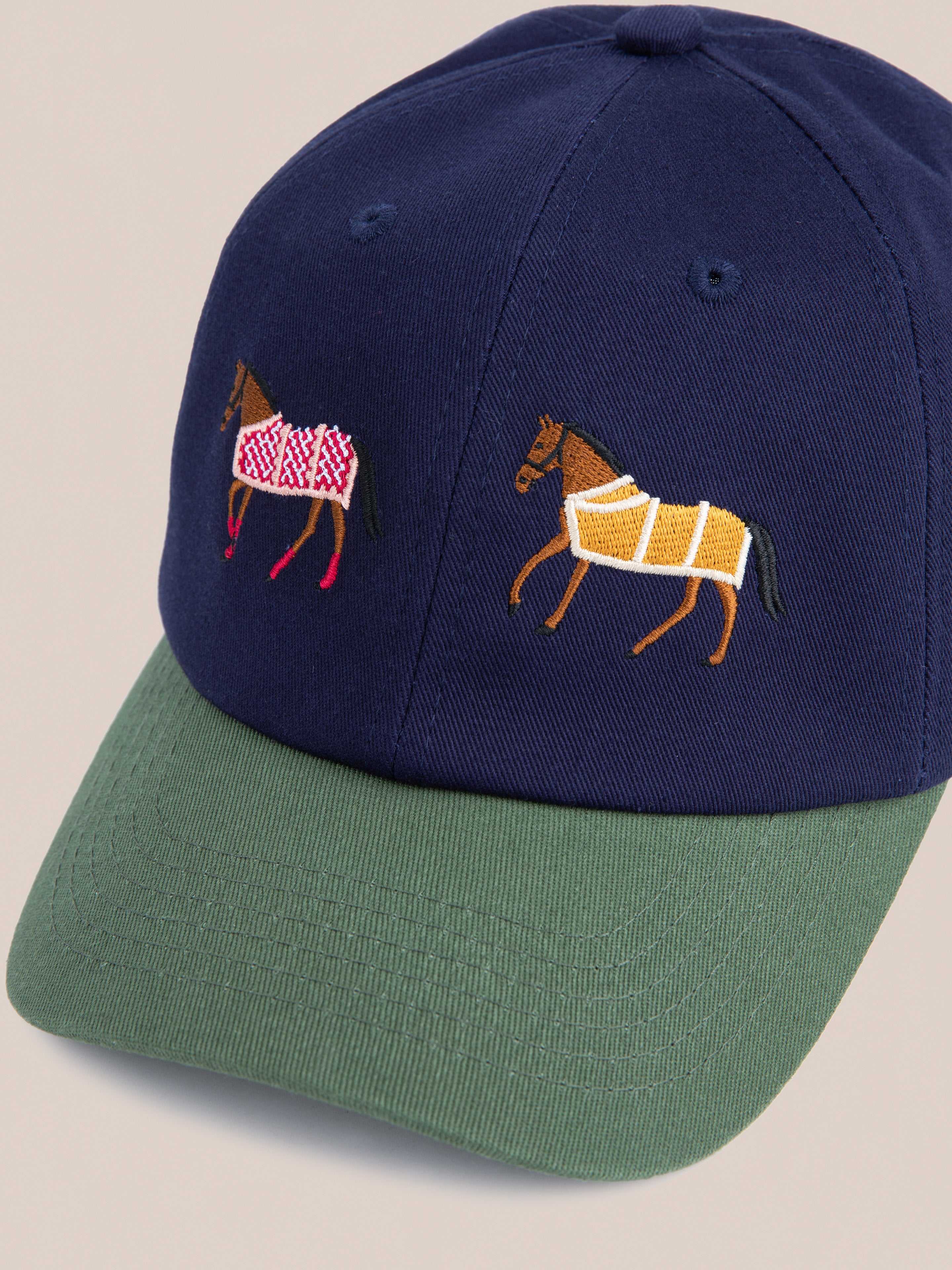 Introducing the Found Horse Equine Cap: a navy blue cap with a green brim, featuring 70's color-blocking and two embroidered horses—one in a red and white blanket, the other in yellow and white.