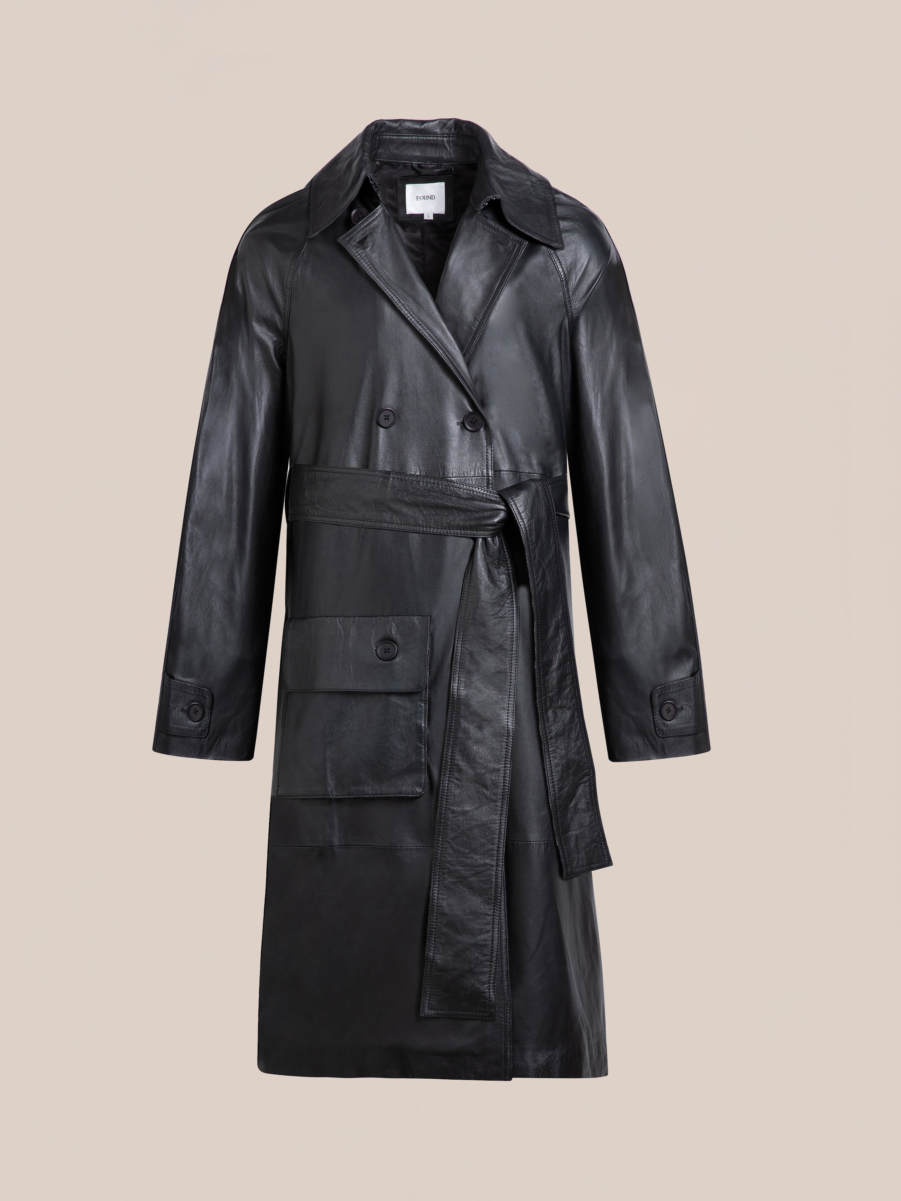 The FOUND Leather Trench Coat features a waist belt, double-breasted front, and large patch pocket. Ethically crafted from luxurious cowhide leather, it is shown on a plain beige background.