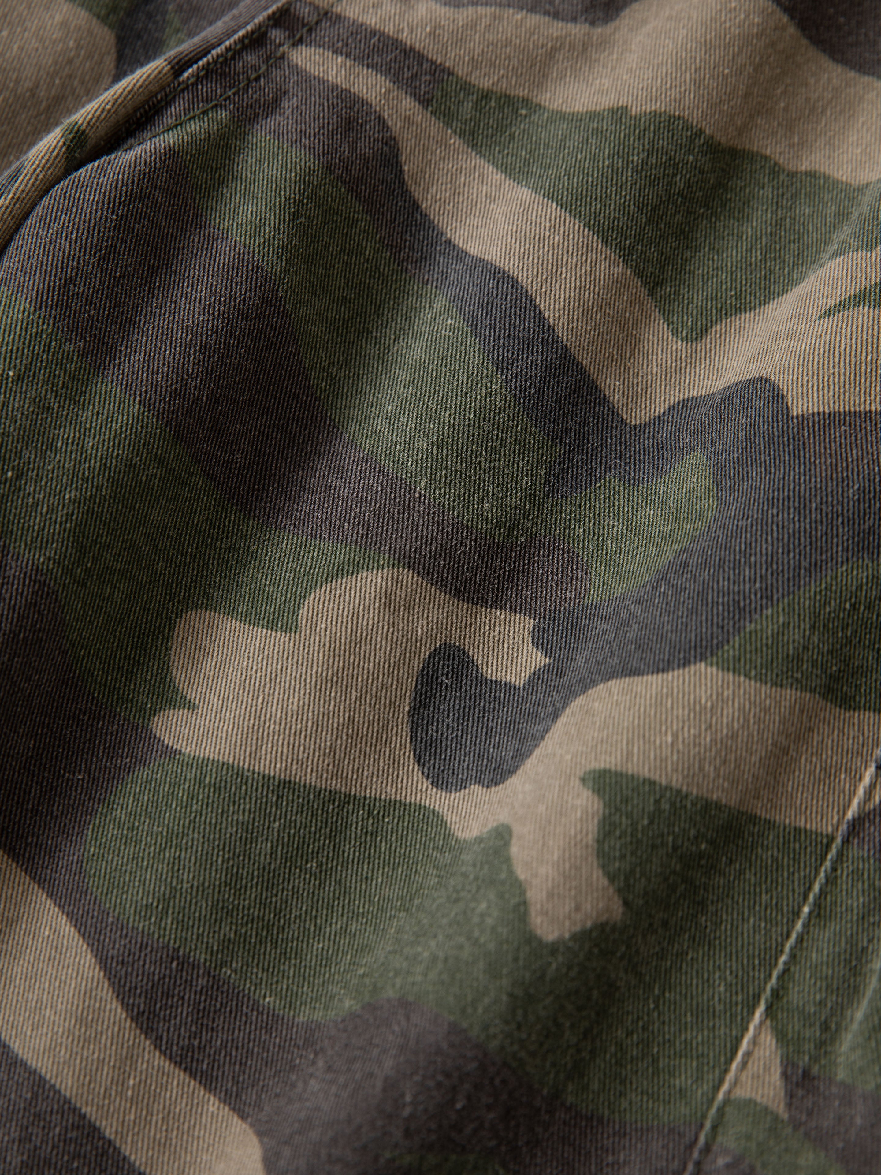 Close-up of the Camouflage Twill Utility Cargo Shorts by FOUND, featuring green, brown, and beige camo fabric with a visible seam for a vintage look.