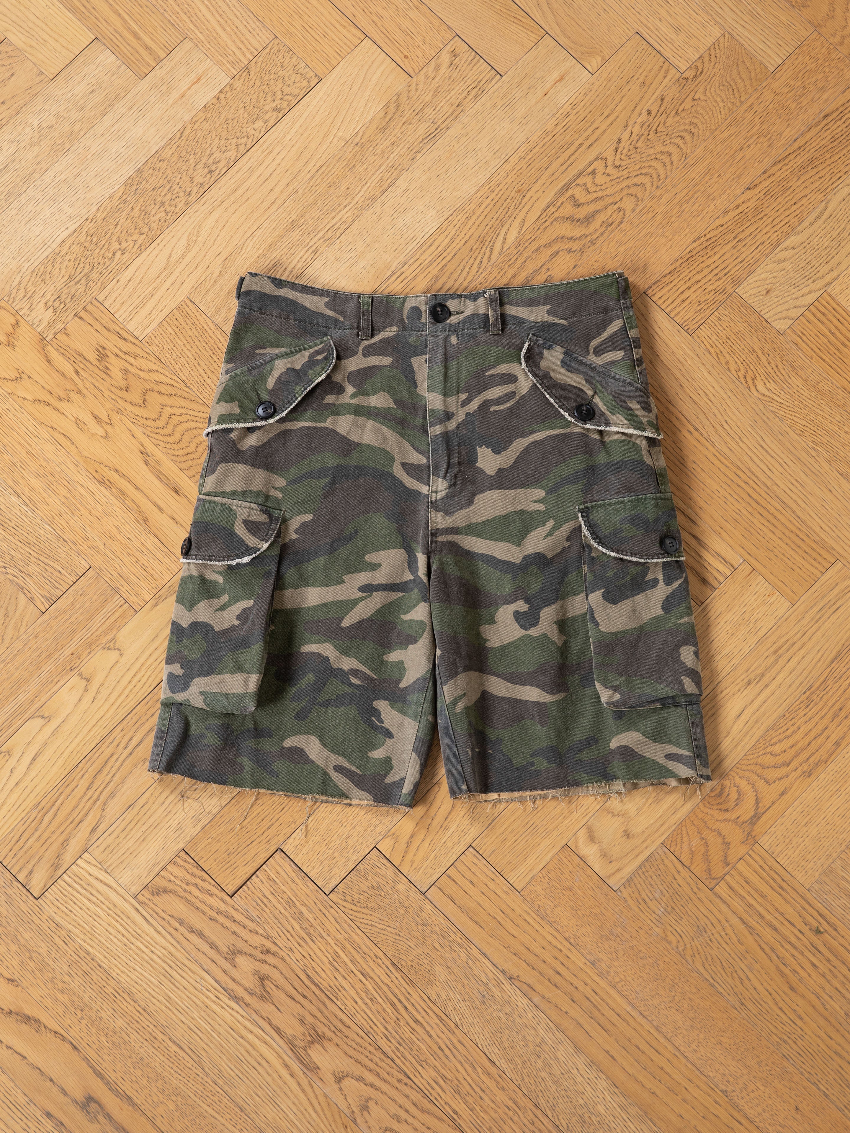 FOUND Camouflage Twill Utility Cargo Shorts in a relaxed unisex fit are laid flat on a wooden parquet floor, highlighting their stylish vintage look and multiple utility pockets.