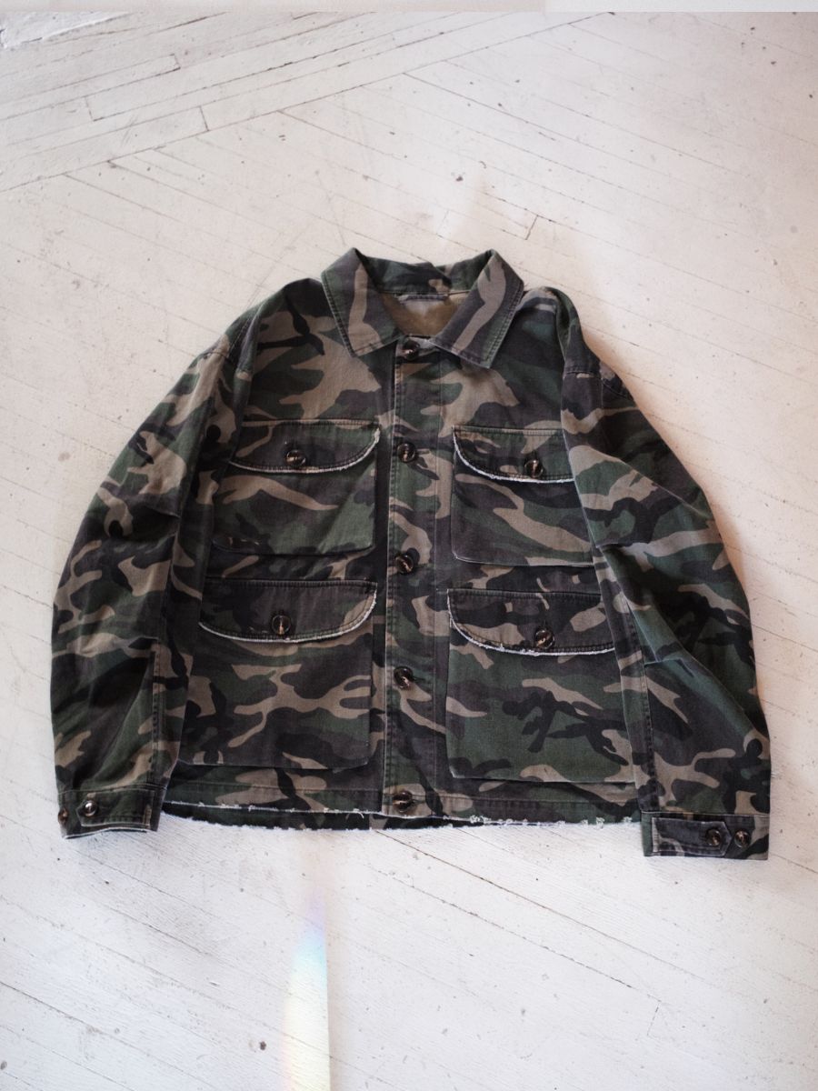 The FOUND Camouflage Twill Utility Cargo Jacket, made from midweight cotton twill with front pockets and a classic camo design, is laid flat on a light surface.