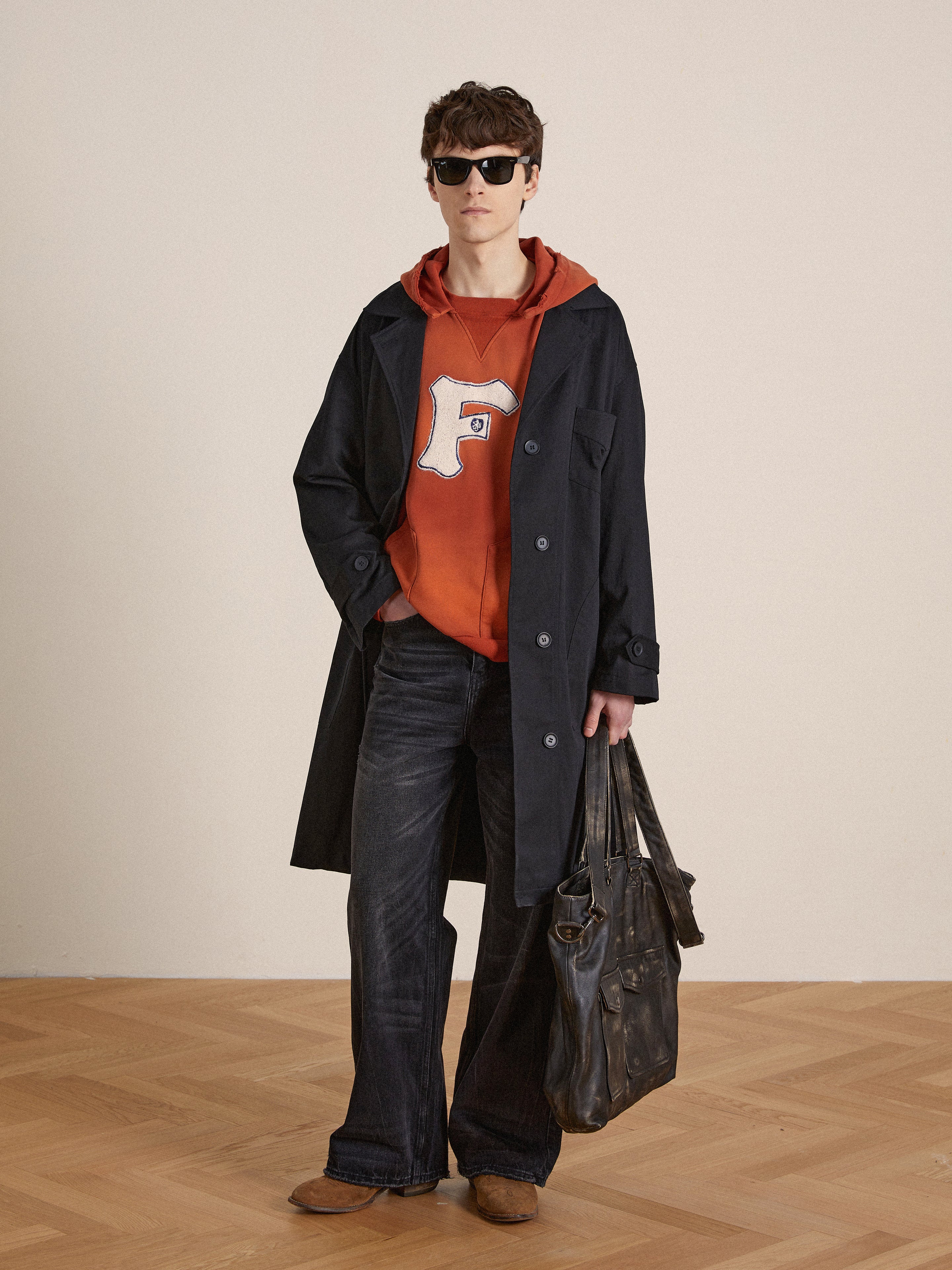 A man in a Found faded "F" hoodie and jeans holding a bag.