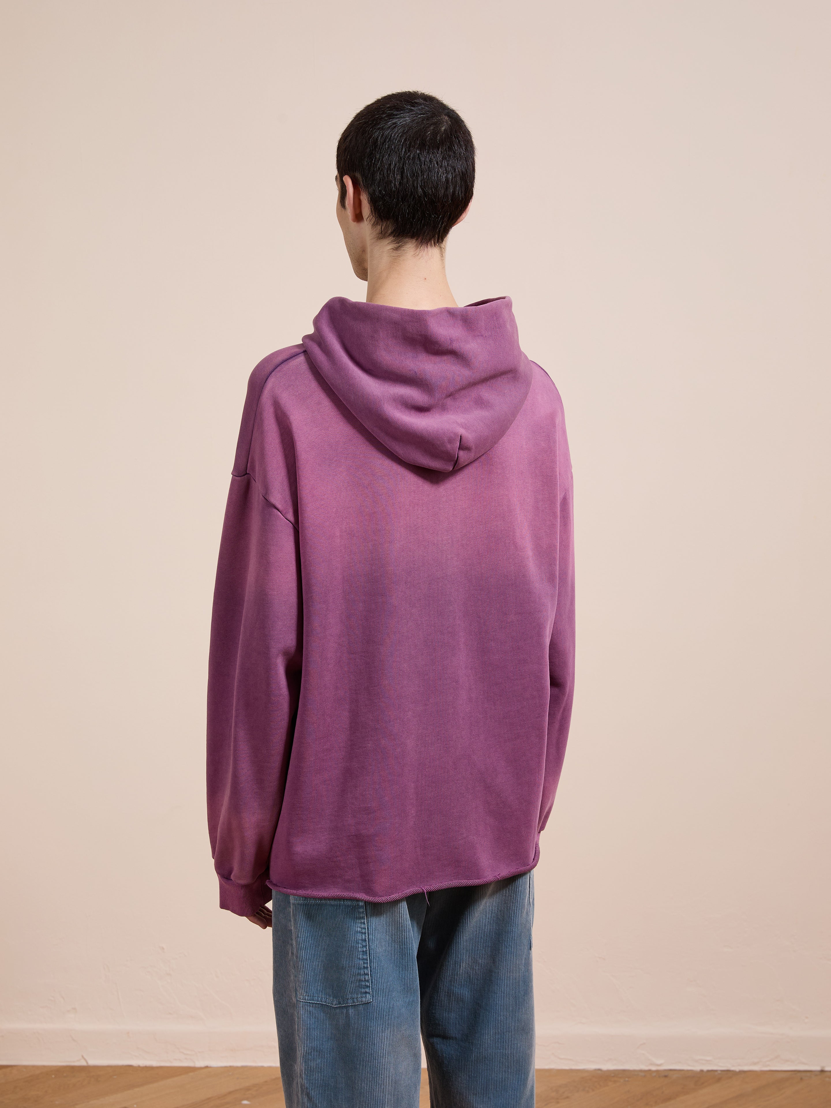 A person stands with their back to the camera, wearing a FOUND Embroidered Wildlife Hoodie and blue jeans against a plain beige background.