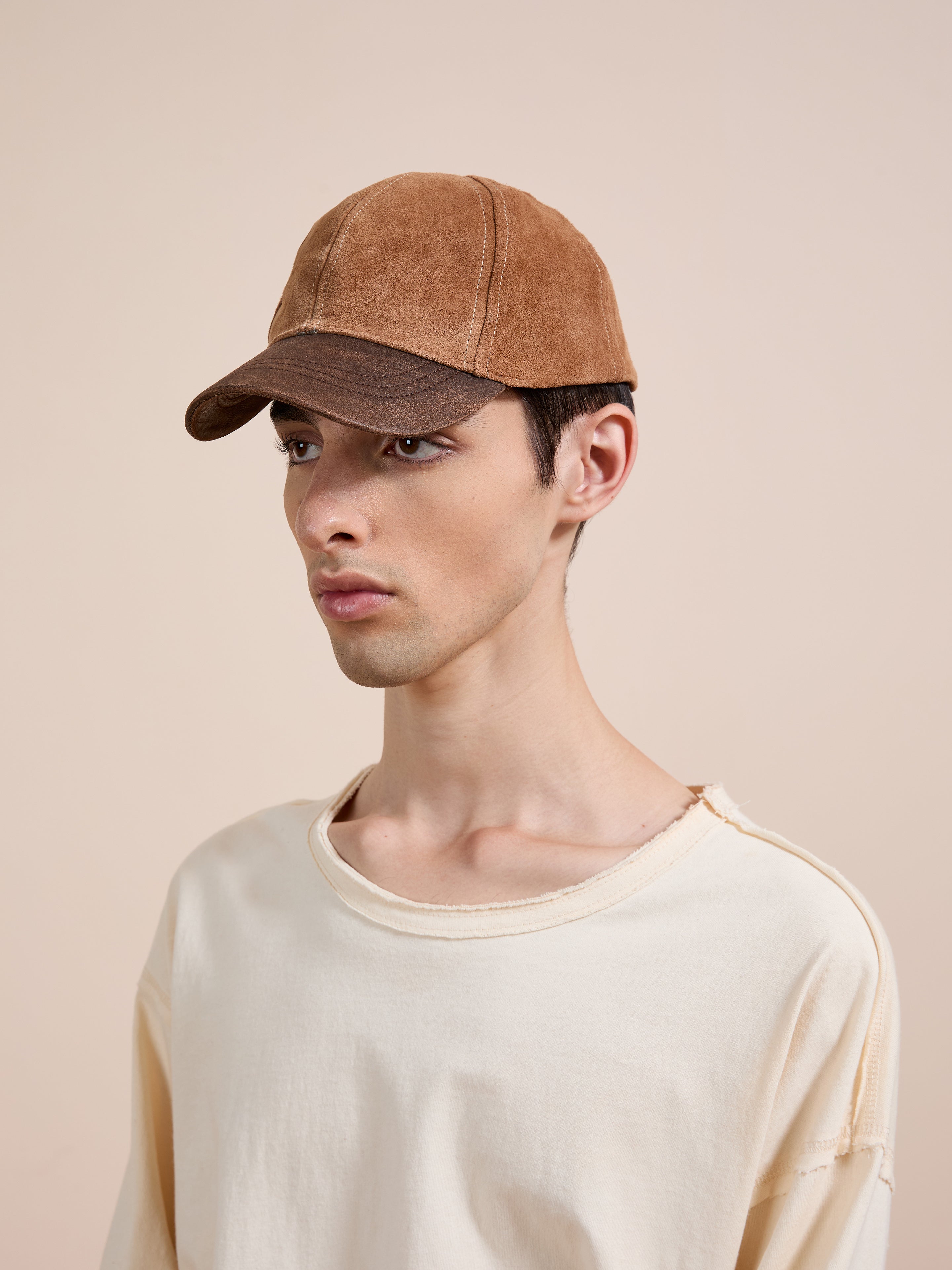 A young person wearing the Found Suede Leather Contrast Distressed Cap and a cream distressed tee stands against a plain beige background.
