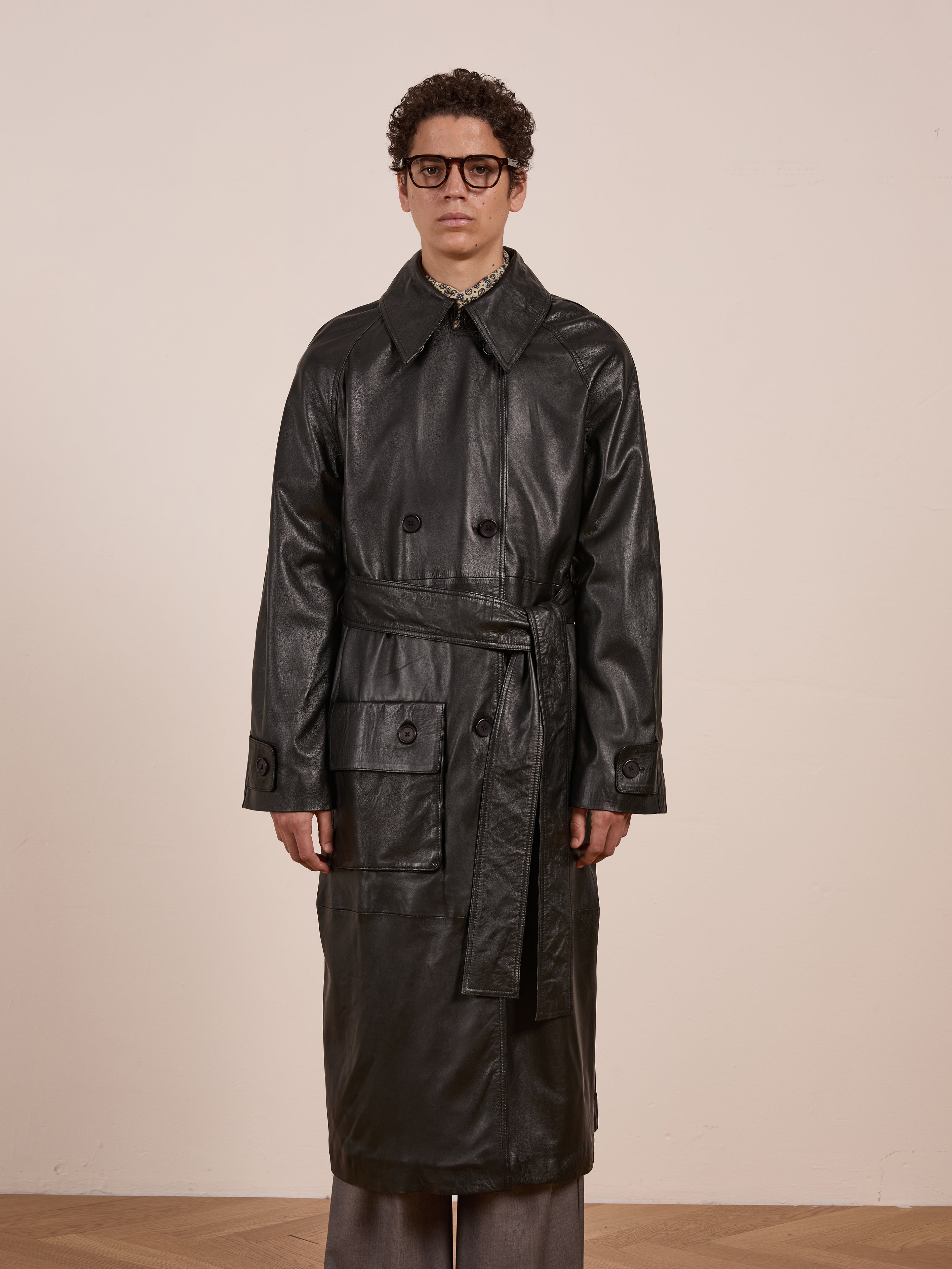 A person wearing glasses models the FOUND Leather Trench Coat, standing forward against a plain light background.