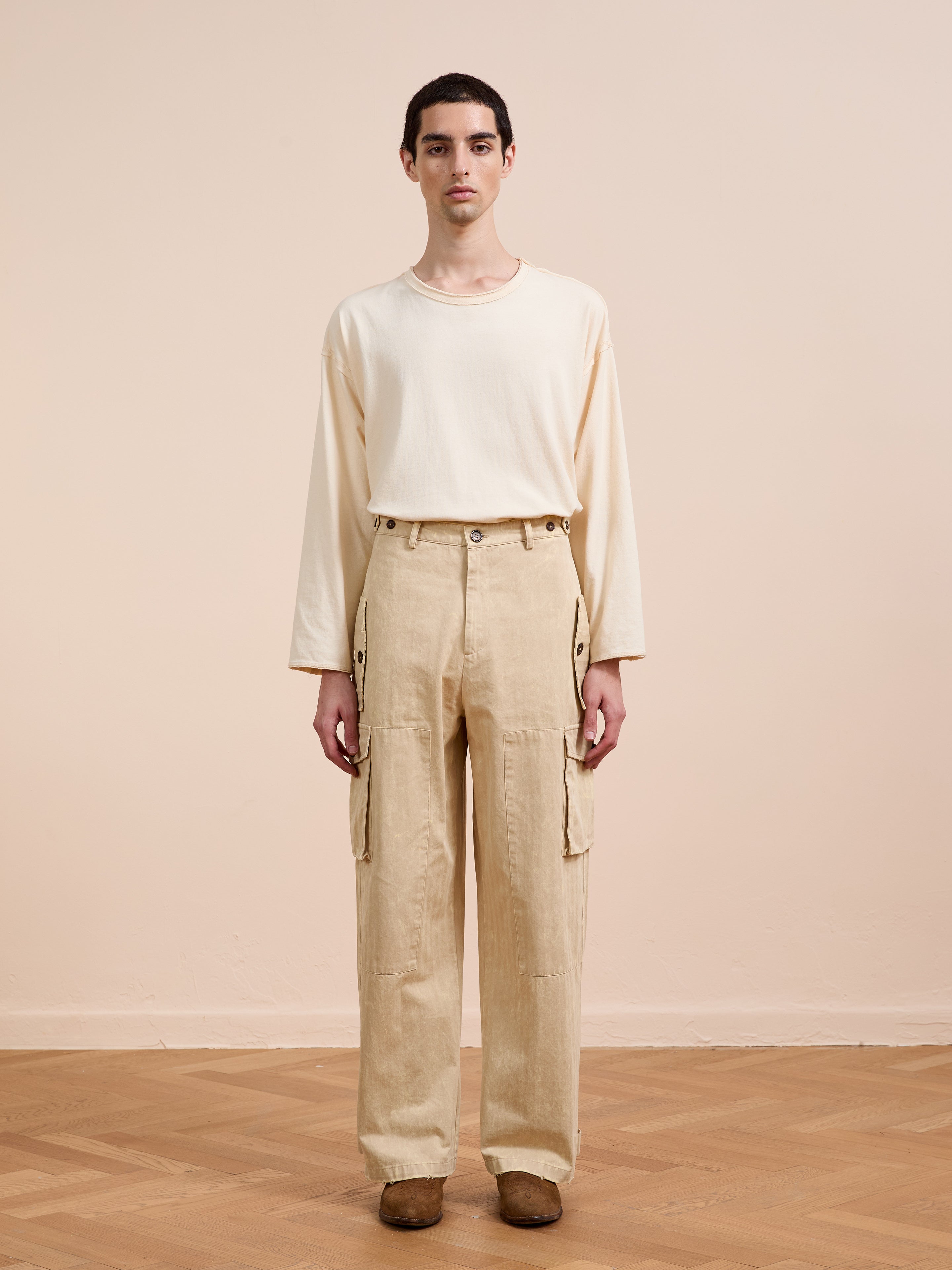 A person stands indoors in a loose cream long-sleeve shirt and FOUND Utility Herringbone Paneled Pants, styled with brown shoes against a light background for a modern utility wear look.