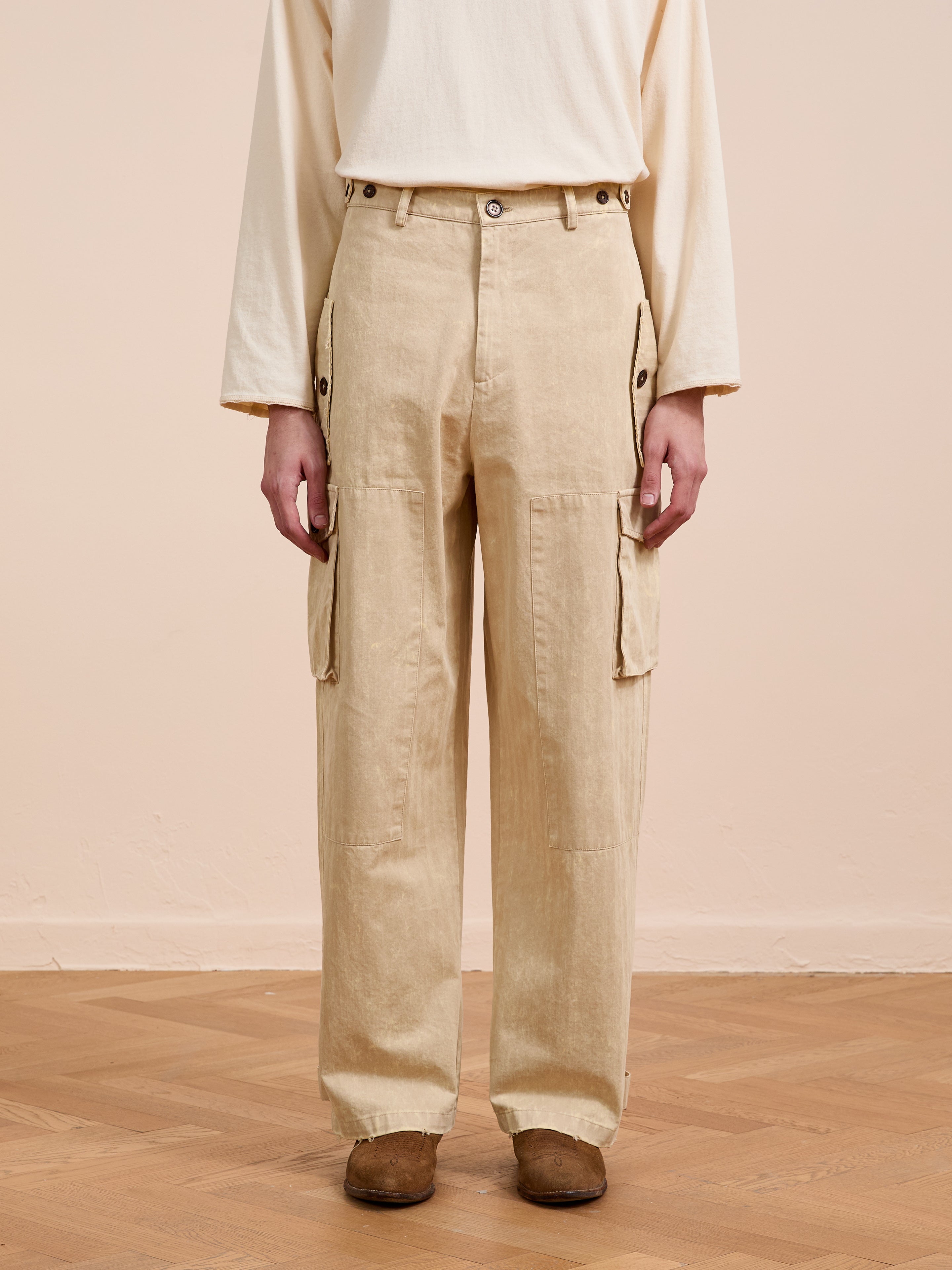 A person stands on a wooden floor against a plain light background, showcasing FOUND's Utility Herringbone Paneled Pants styled with a cream long-sleeve shirt and brown shoes for a modern utility look.