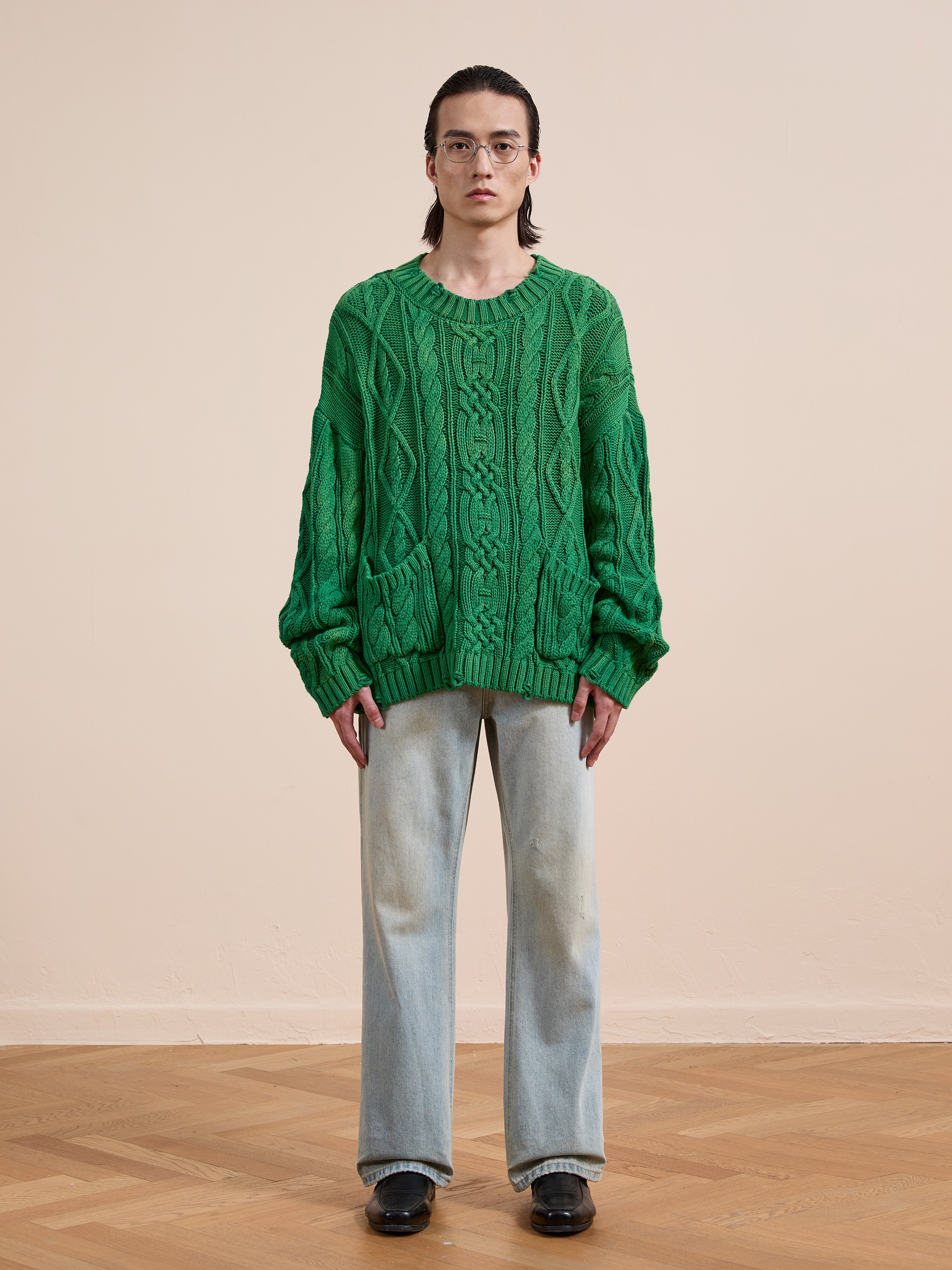 Model wears the Found Cable Knit Pullover Sweater with light blue wide-leg jeans and black shoes, standing on a wooden floor against a plain beige wall.