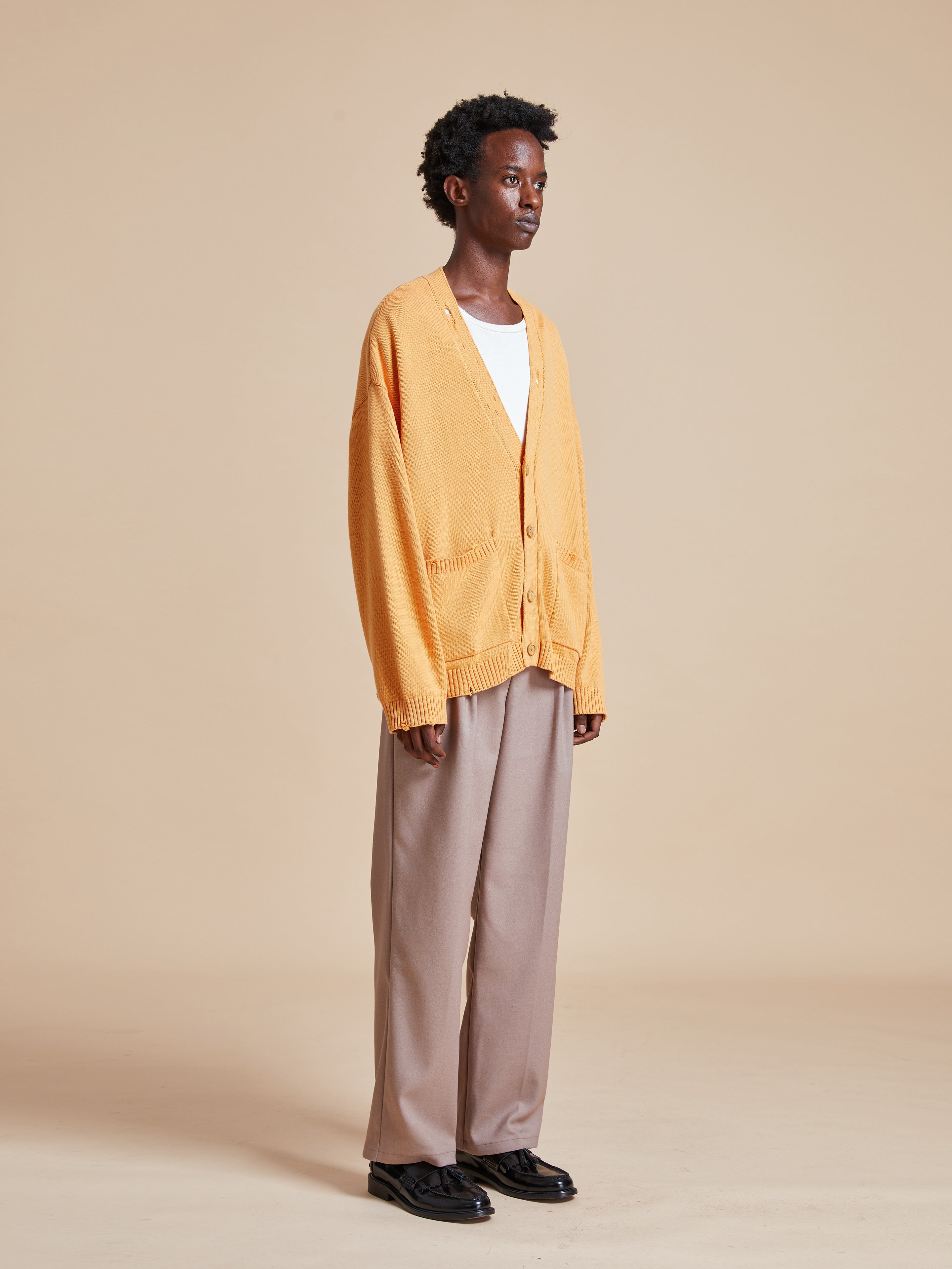 The model is wearing a Cadmium Distressed Cardigan from Found and tan pants.