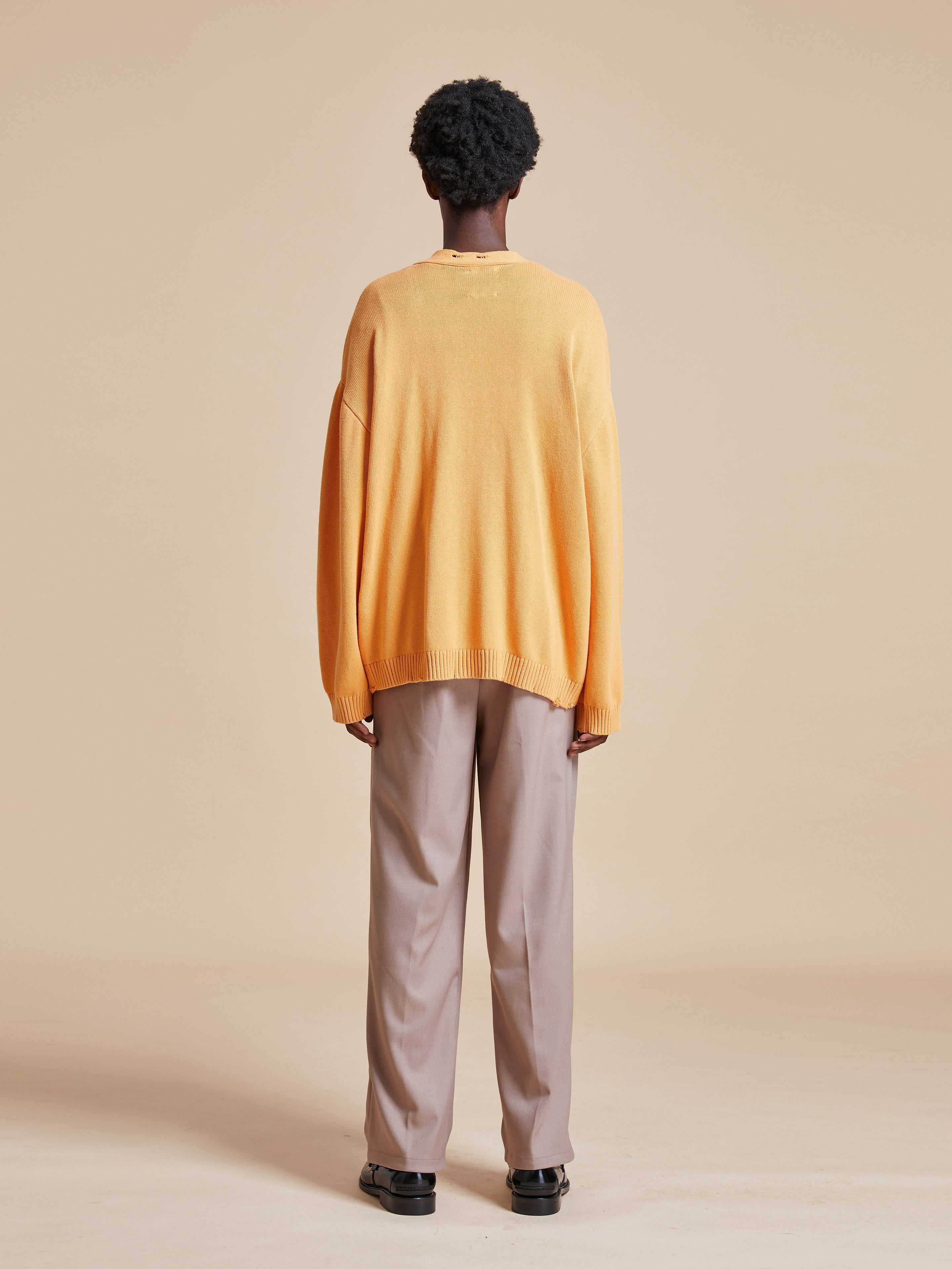 The back view of a man wearing a Found Cadmium Distressed Cardigan and beige pants.
