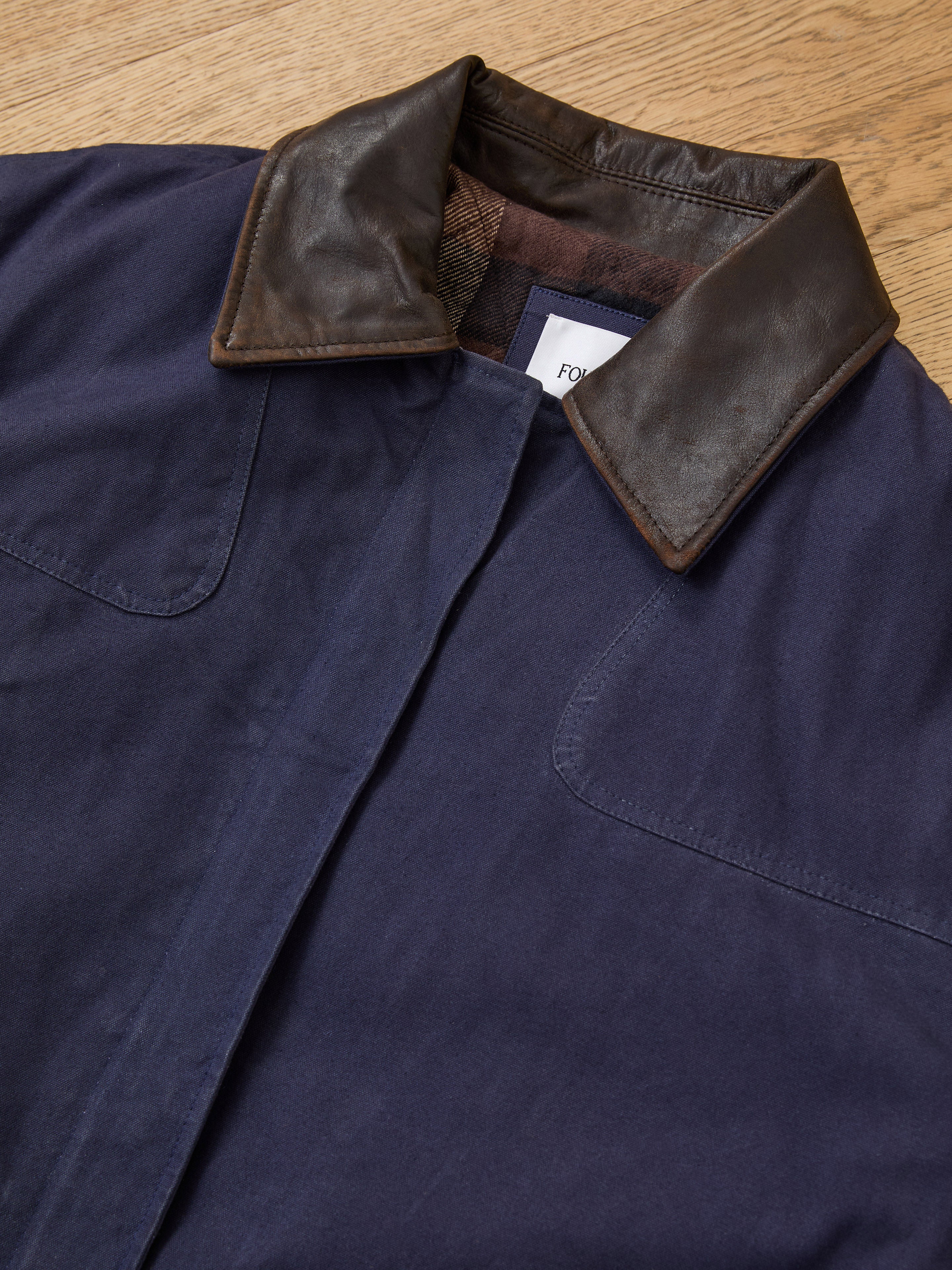 The Found Canvas Distressed Barn Jacket, shown on a wooden surface, features a unisex relaxed fit and a distressed leather collar for versatile style.