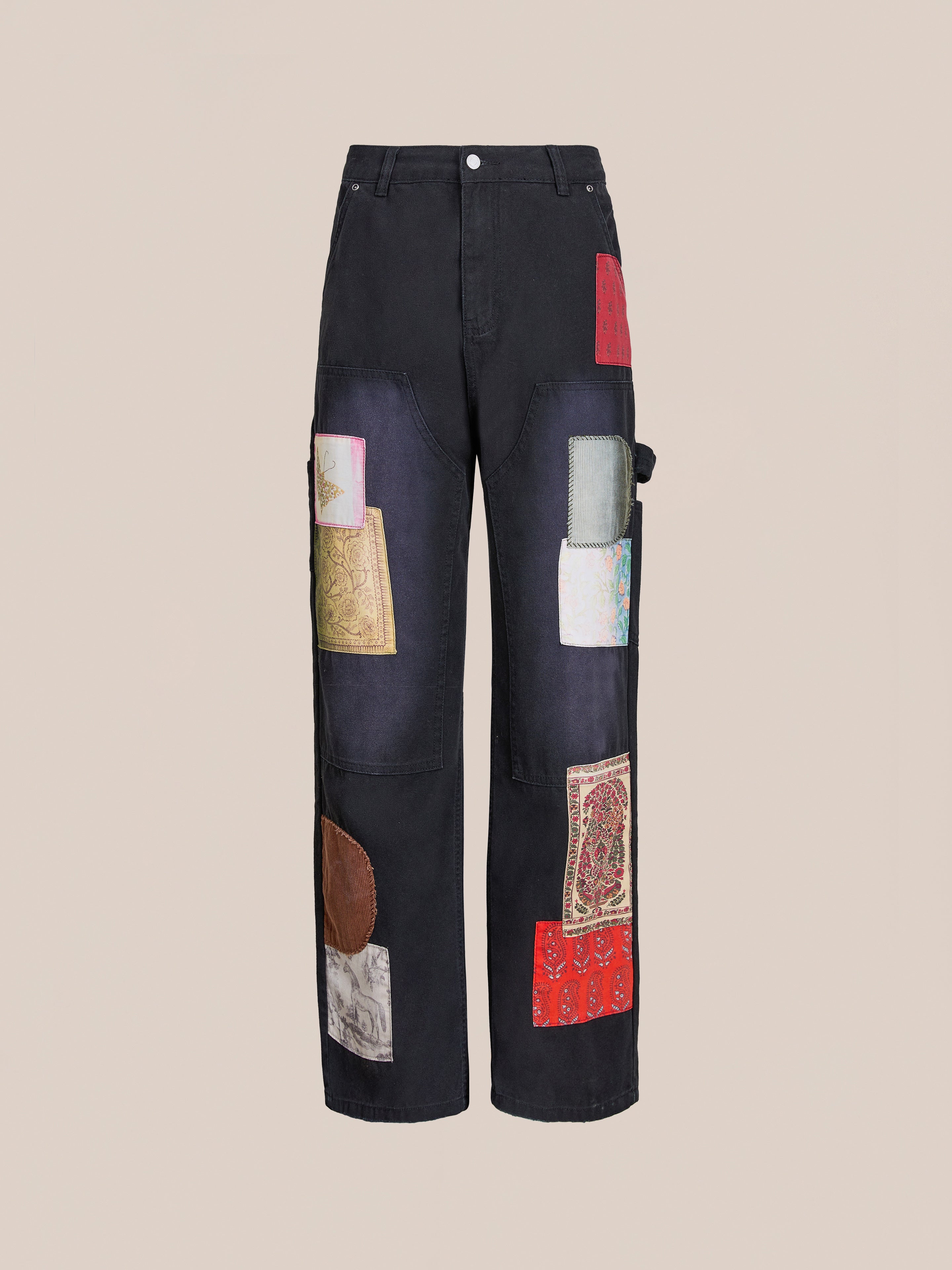 The FOUND Tapestry Carpenter Canvas Pants are black wide-leg pants featuring colorful fabric patches inspired by Pakistani quilts and artisan craft, shown against a plain beige background.