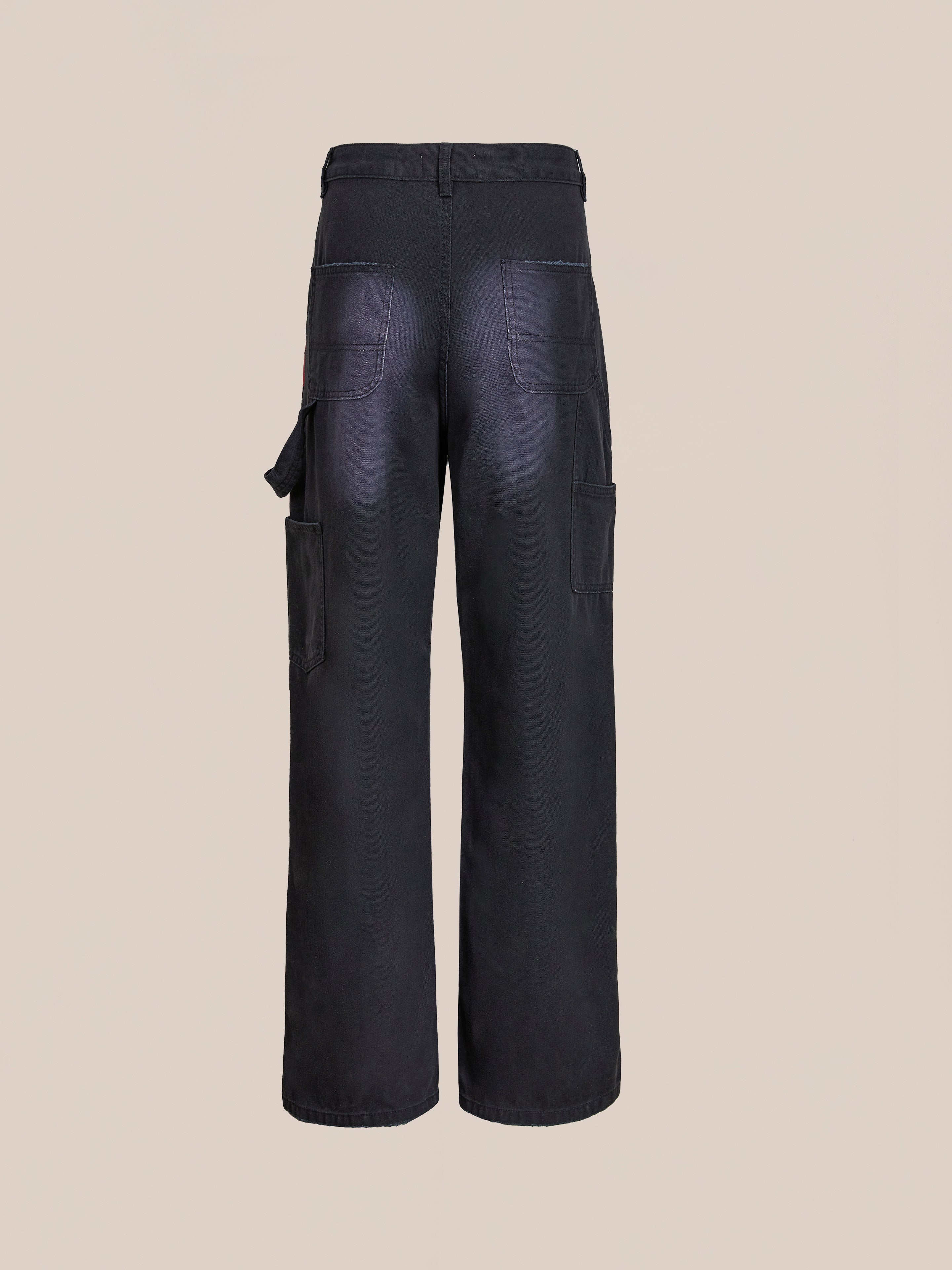 FOUND Tapestry Carpenter Canvas Pants feature a black printed design, wide legs, multiple pockets, and a hammer loop, shown from the back on a plain beige background.