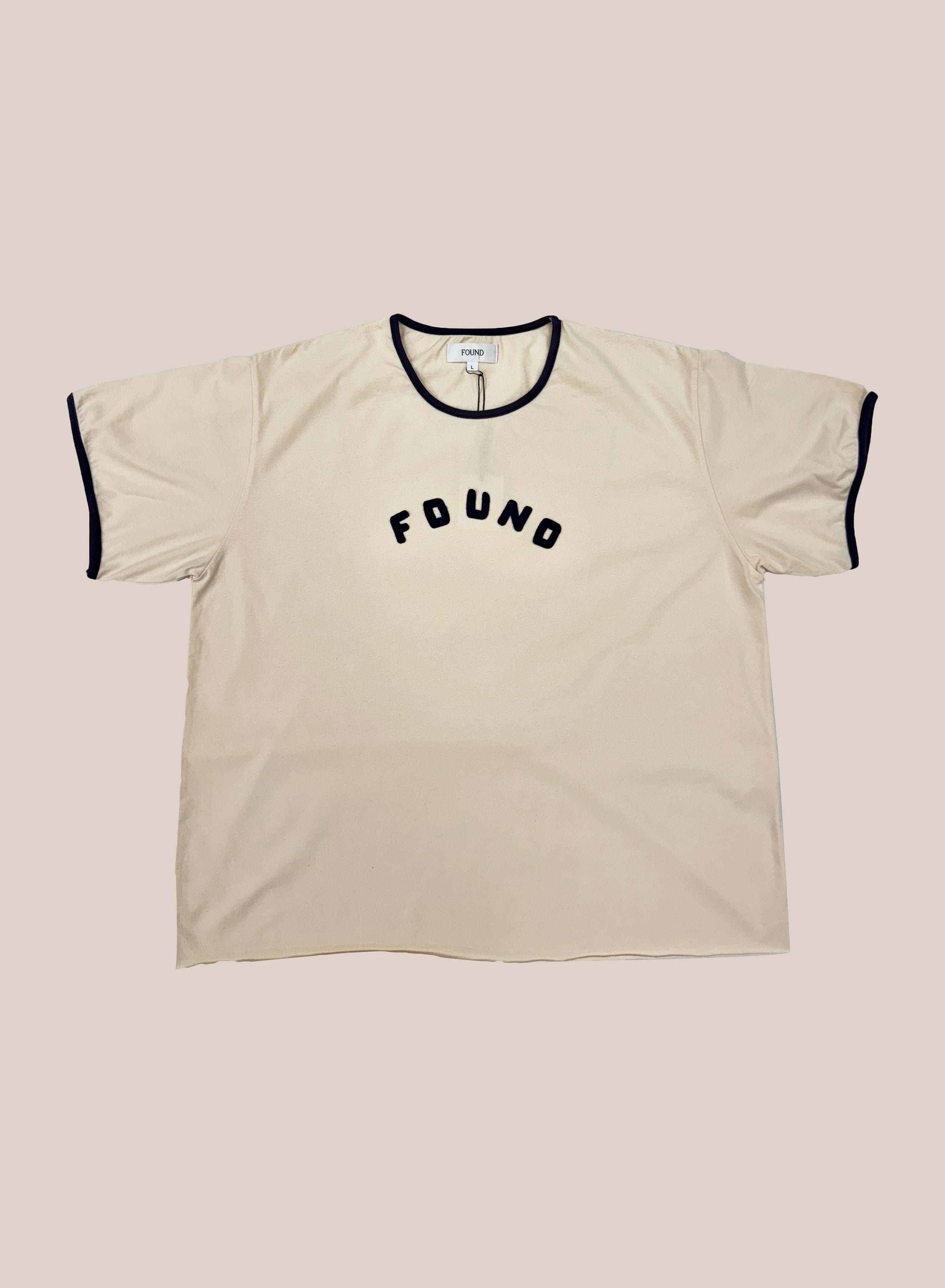 The FOUND Logo Felt Patch Ringer Tee is a beige, vintage-inspired unisex shirt with black trim and "FOUND" in bold on the chest, offering relaxed comfort and timeless style.
